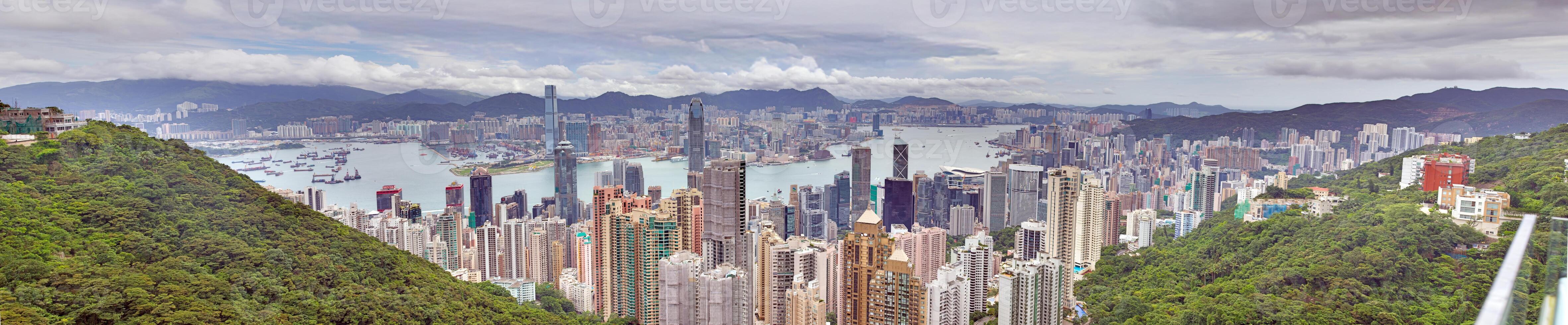 Panoramic daytime view of Hong Kong skyline, surrounded by lush green hills and a busy harbor photo