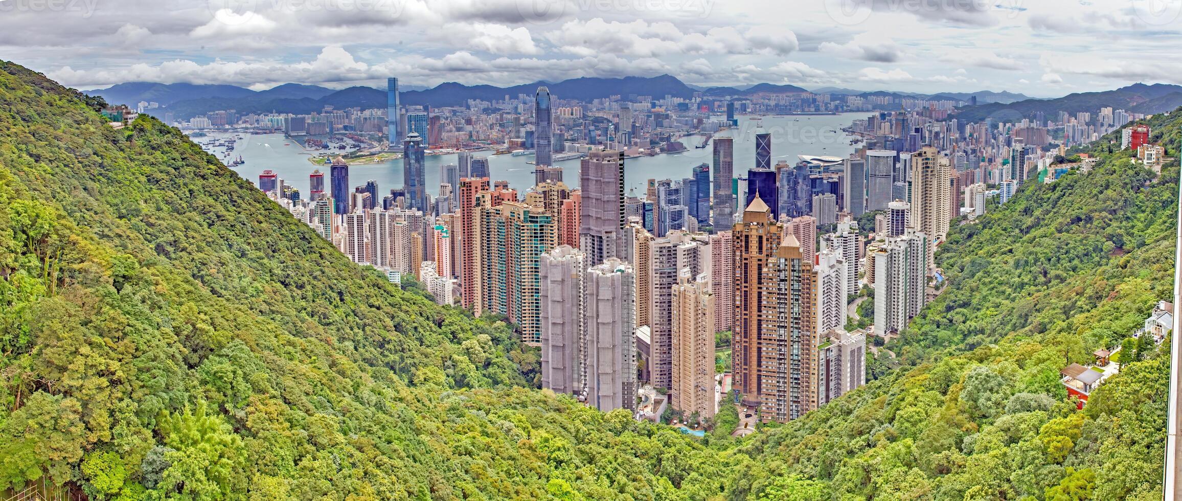 Panoramic daytime view of Hong Kong skyline, surrounded by lush green hills and a busy harbor photo