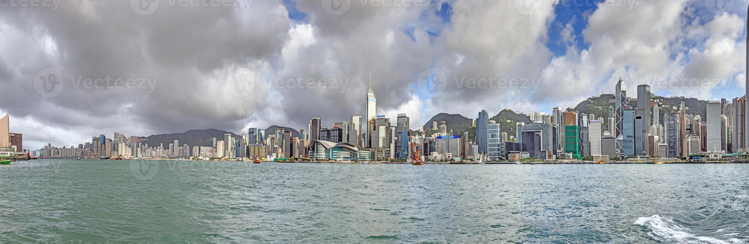 Panoramic daytime view of Hong Kong skyline, surrounded by lush green hills and a busy harbor photo