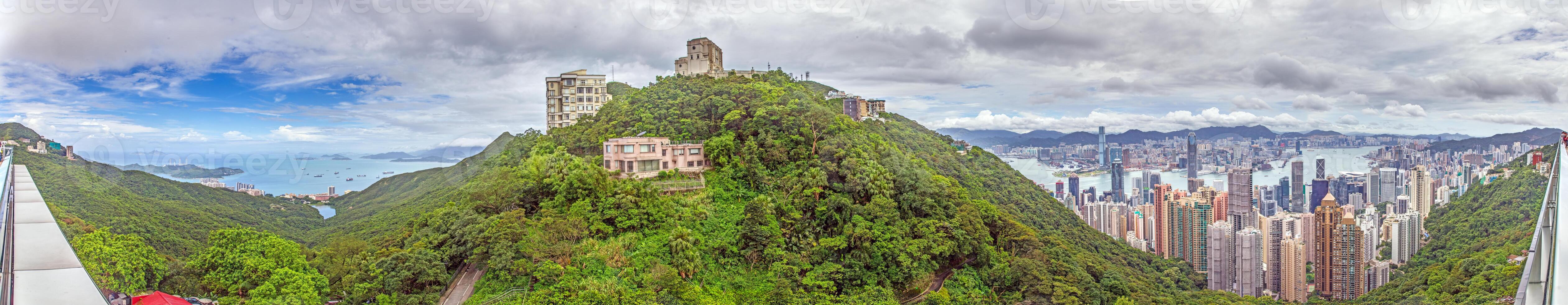Panoramic daytime view of Hong Kong skyline, surrounded by lush green hills and a busy harbor photo
