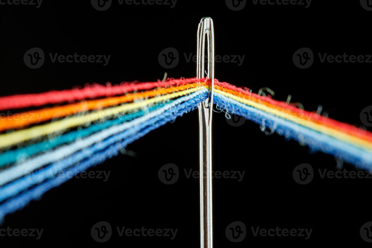 multi-colored threads for sewing in the form of a rainbow pass through an antique needle on a black background photo