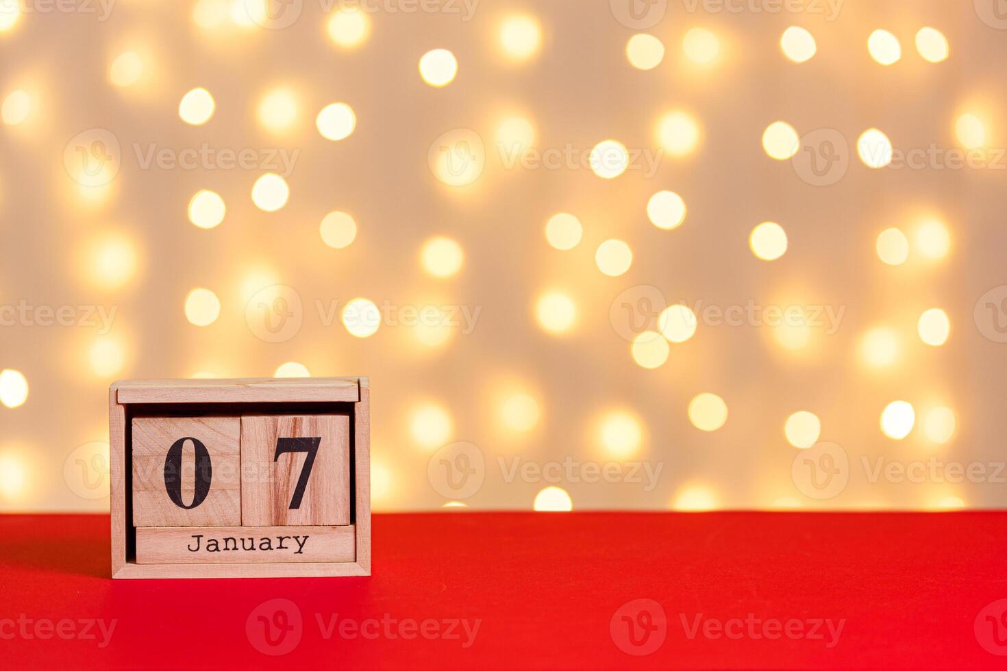 christmas, wooden calendar january 7 on red background and lights background photo
