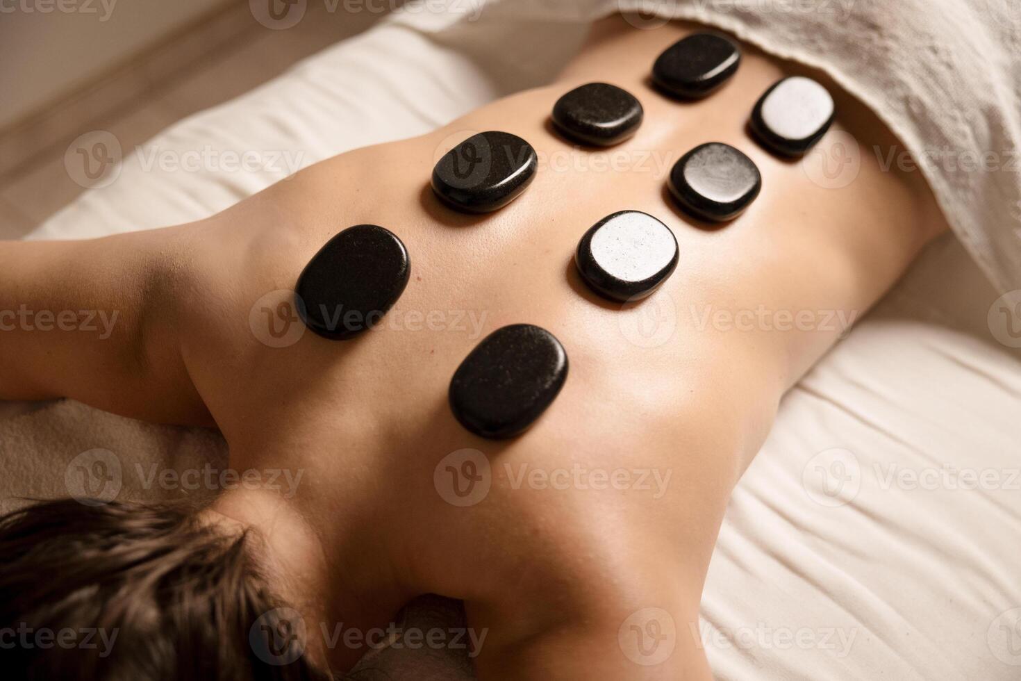 Close up of hot stones placed on the back during a spa therapy session. Hot stone massage and wellness concept photo