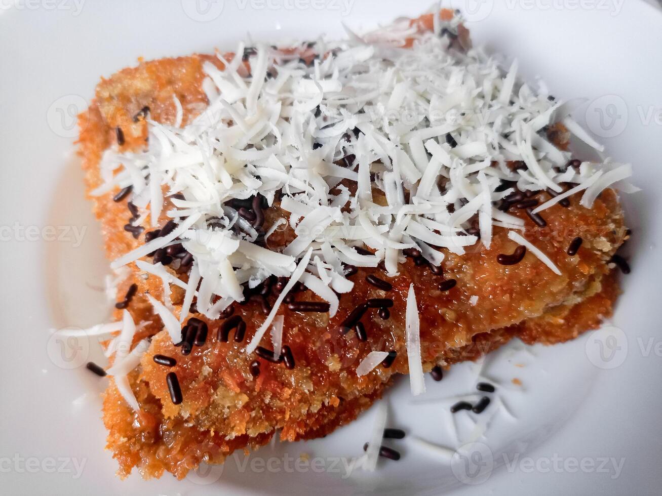 Pisang Bakar Coklat Keju or Grilled Banana Chocolate Cheese serve with chocolate sprinkles and cheddar cheese graters on white plate. photo
