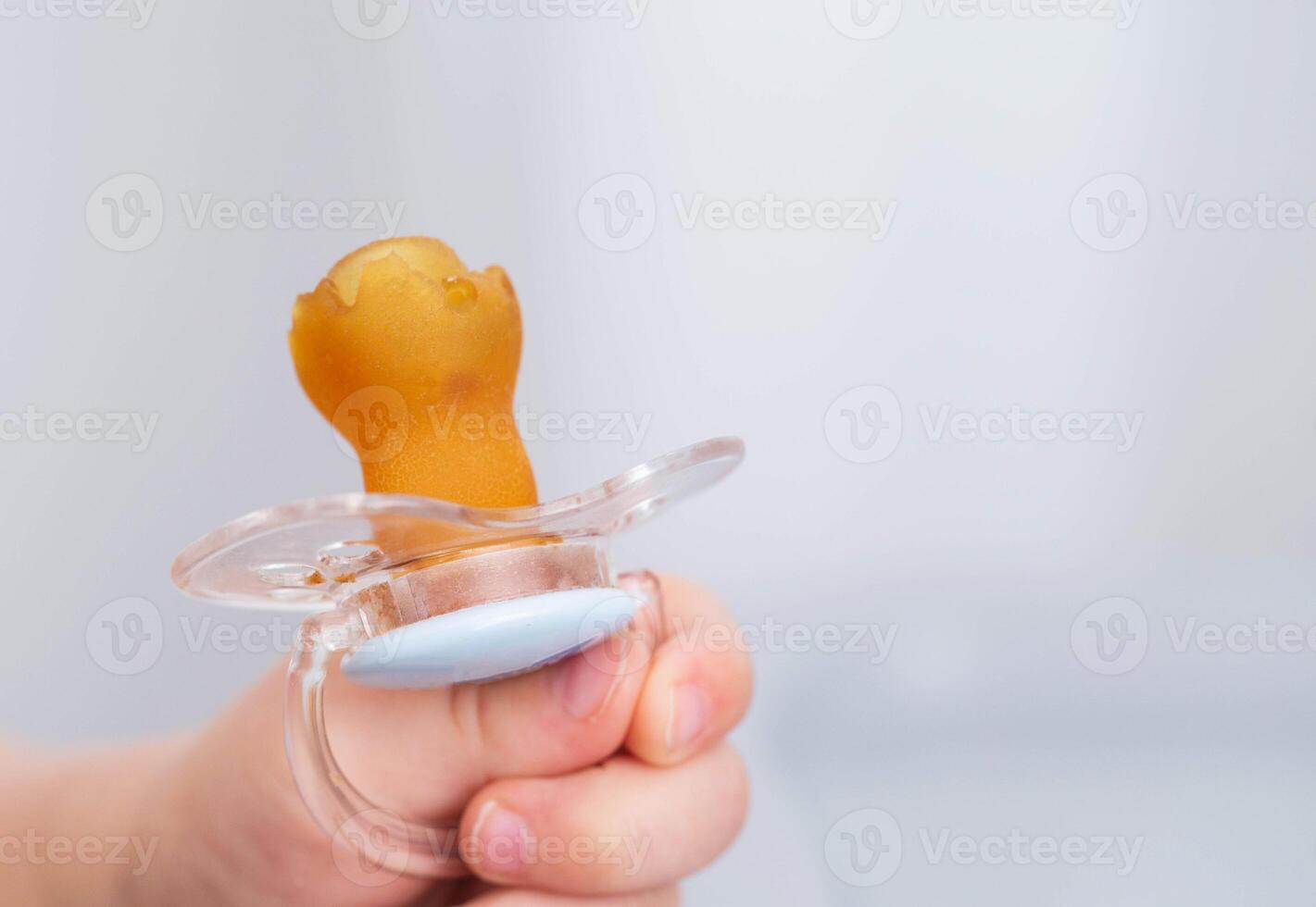 The baby is holding a torn and chewed silicone pacifier in his hands. Concept of teething in children, sucking reflex. Copy space for text photo