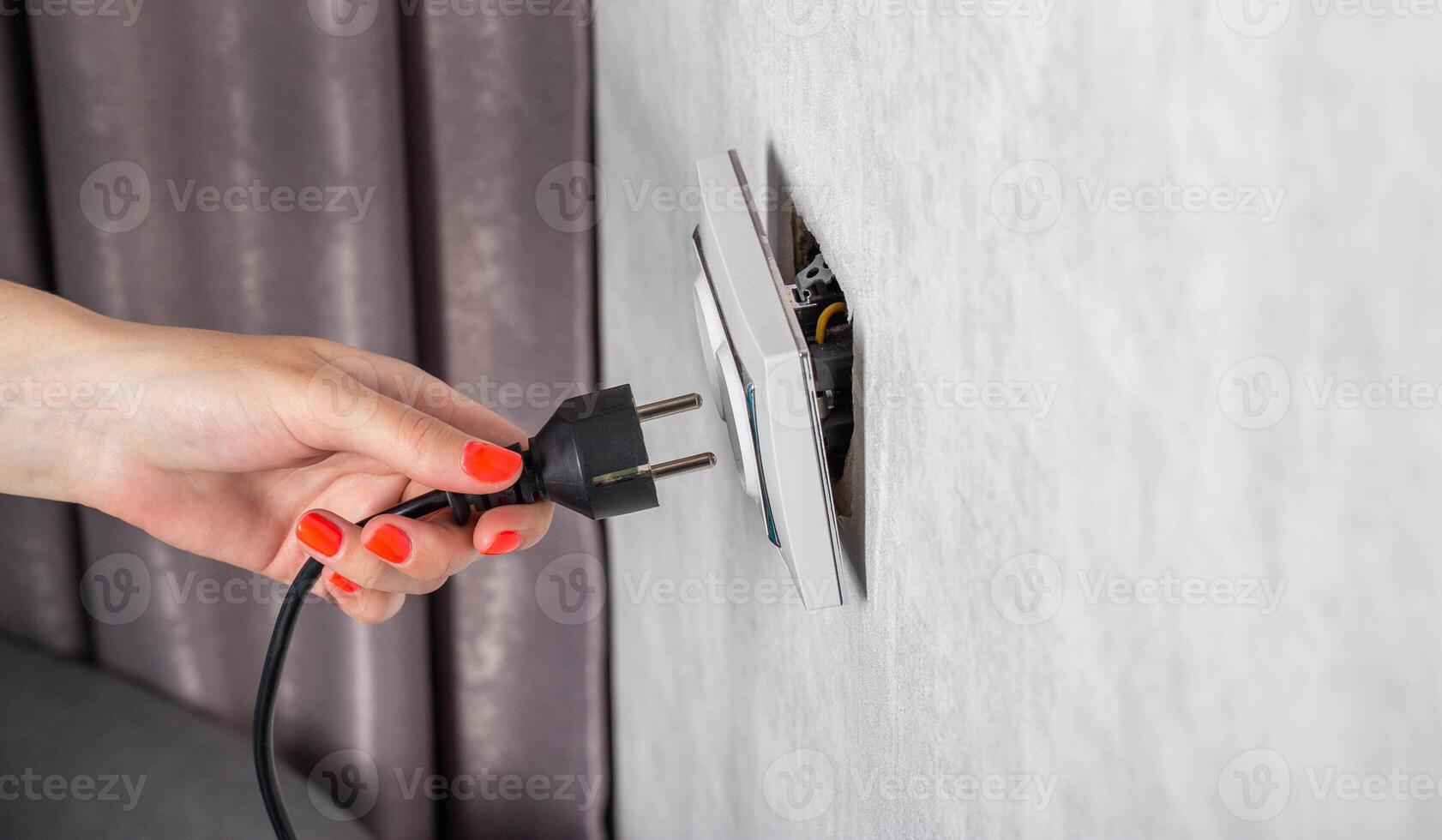 The girl removes the electrical plug from the socket and breaks the socket out of the socket. Incorrect removal of the electrical plug. Risk of electric shock, close-up photo