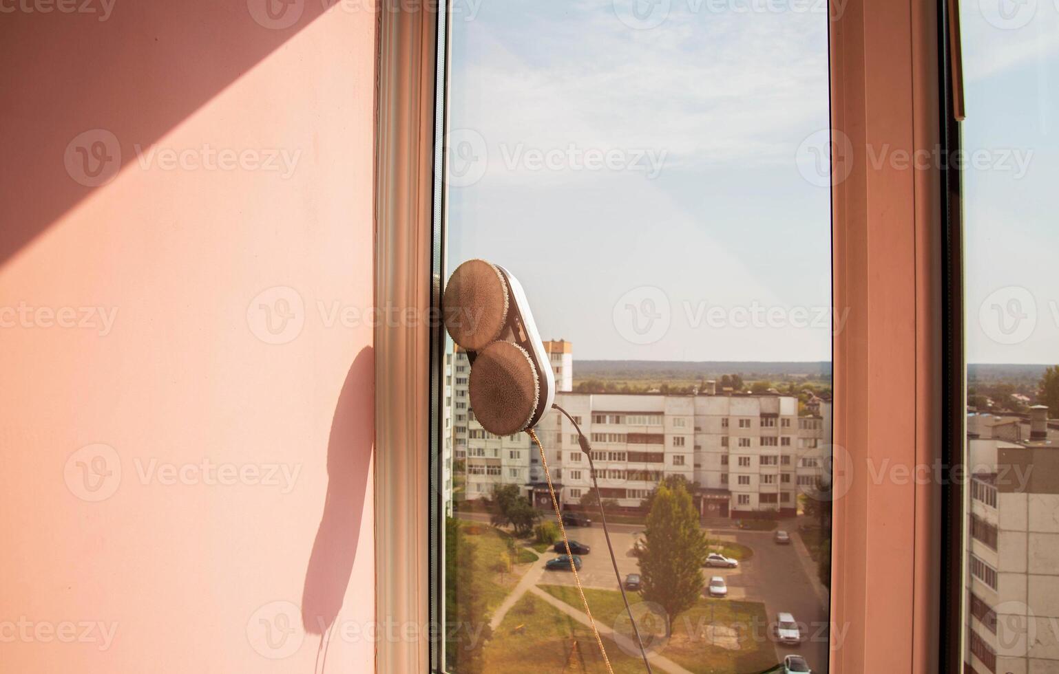 A modern vacuum robot window cleaner washes glass from dirt and stains on a pvc balcony frame. Fall safety. Copy space for text photo