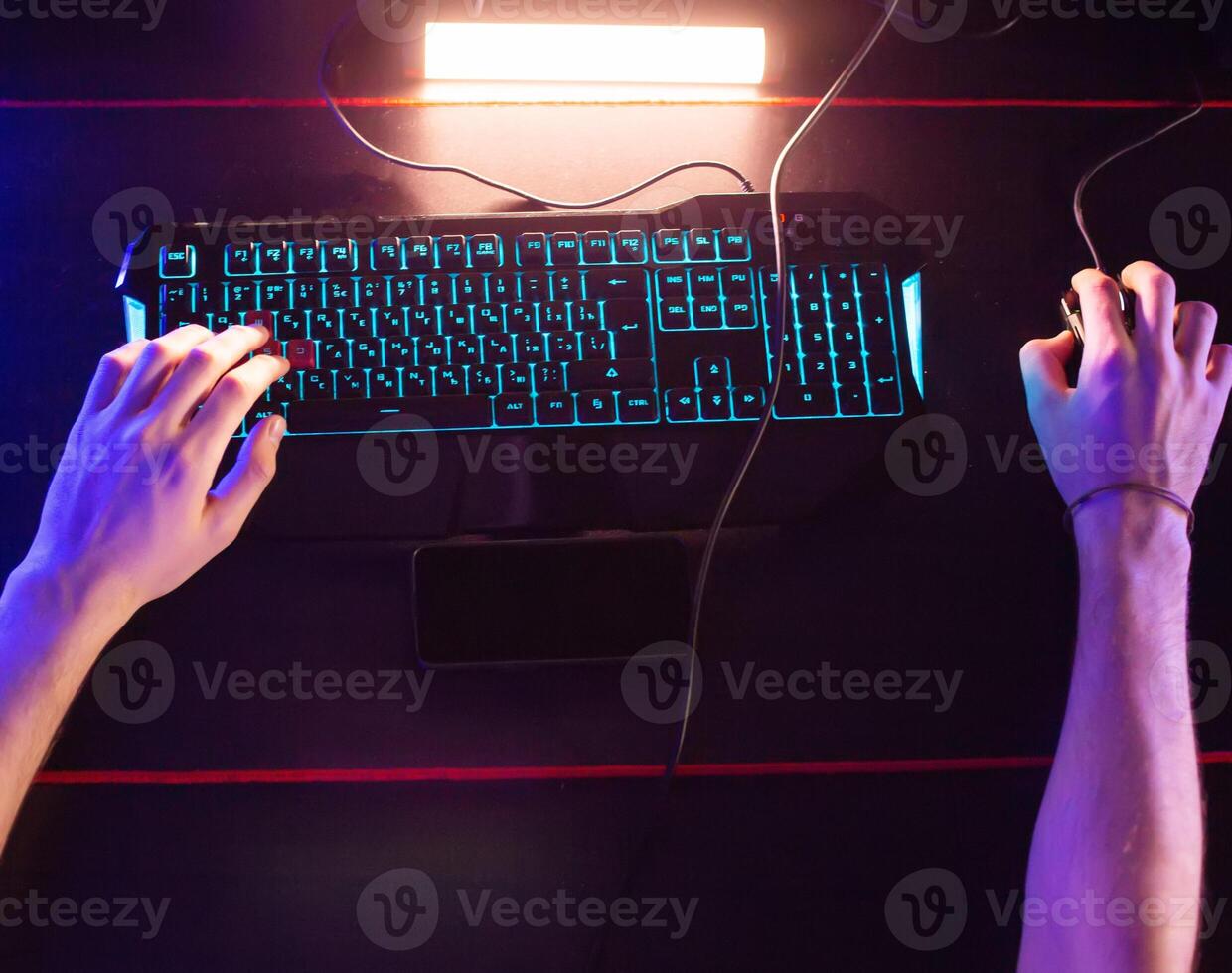 Gamer plays game at computer club, fingers click on buttons of gaming mouse, keyboard with RGB lighting. Professional E-sport tournament, Cyber team. Real-time strategy shooter. Modern equipment photo