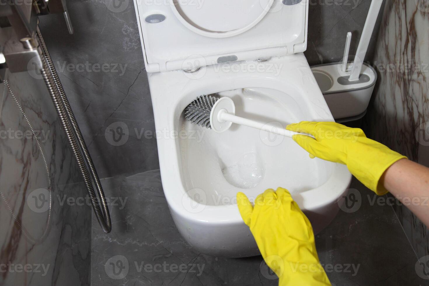 Washing and cleaning the toilet with a brush and detergent to remove dirt, limescale and urinary stone, close-up. Cleaning company services photo