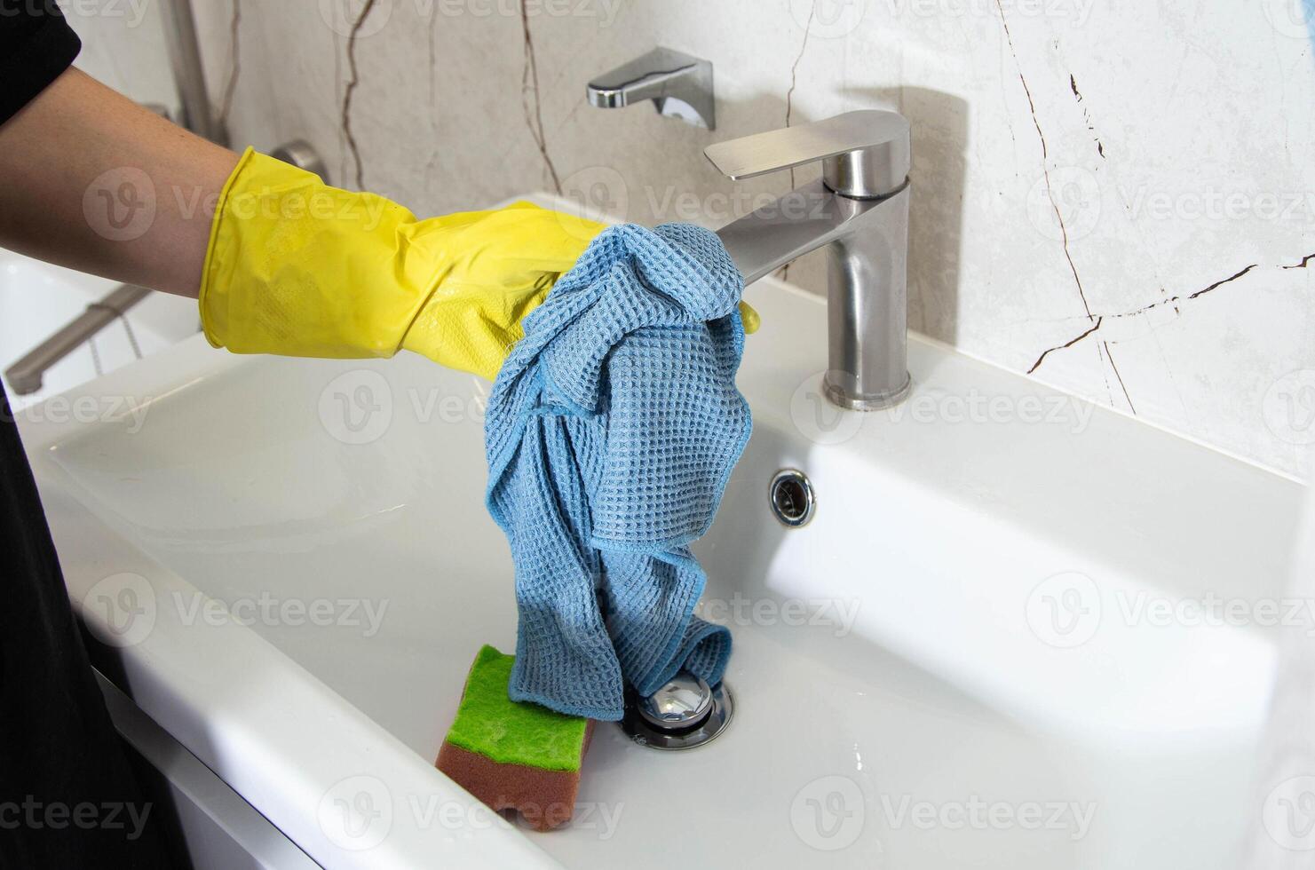 A girl's hands in yellow gloves wash the bathroom sink with a cleaning product for a pleasant smell and shine, close-up. Cleaning company services photo