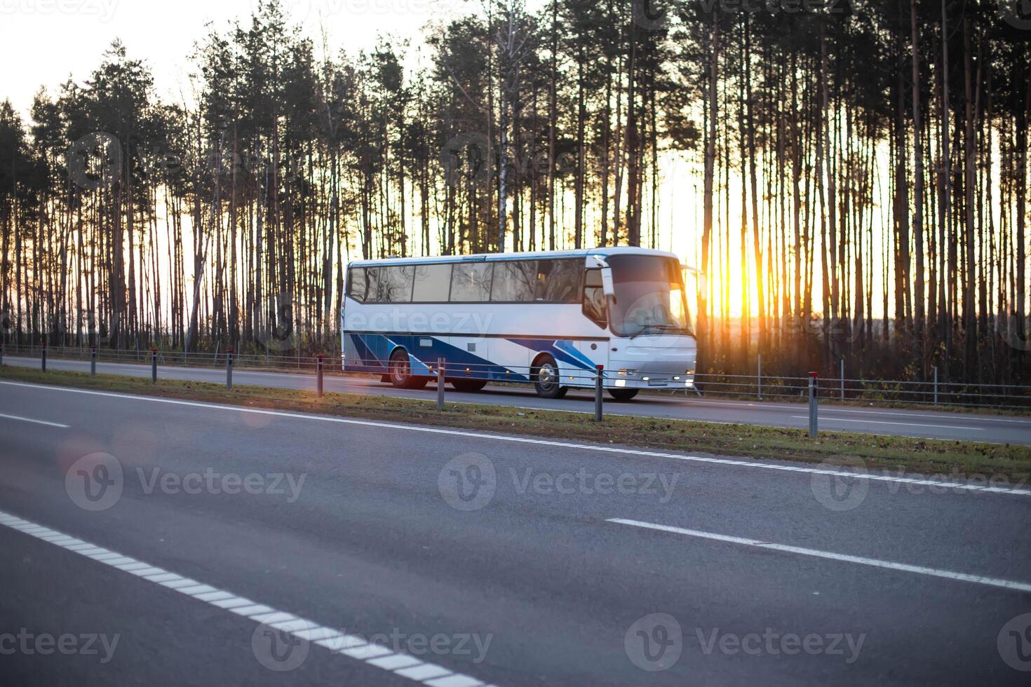 The bus travels along the motorway against the backdrop of a forest and an evening sunset. Passenger transportation concept, vacation trip photo