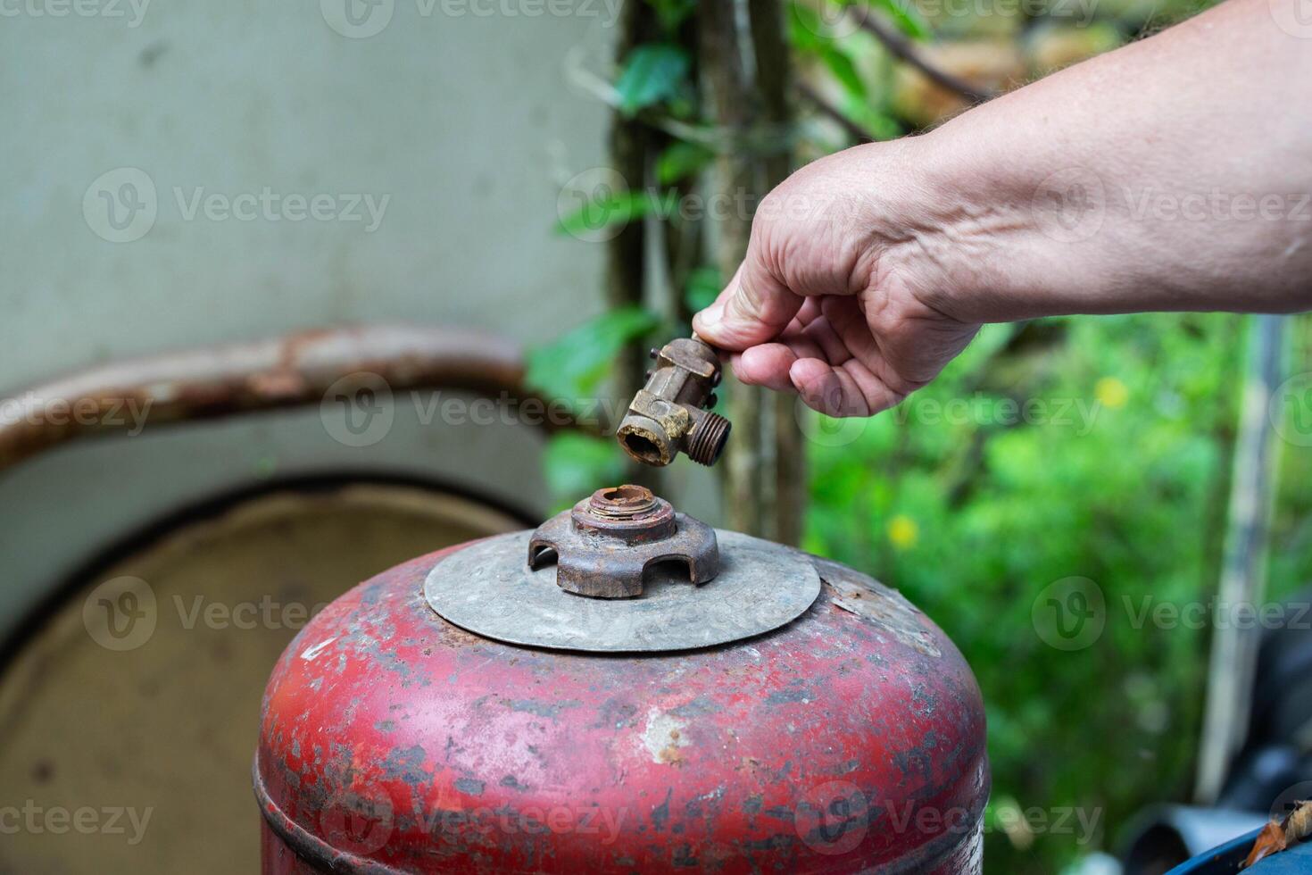 A broken valve of a gas cylinder in a hand against the background of a red gas cylinder. Propane gas leak and explosion concept. Copy space for text, industry. Safety precautions photo