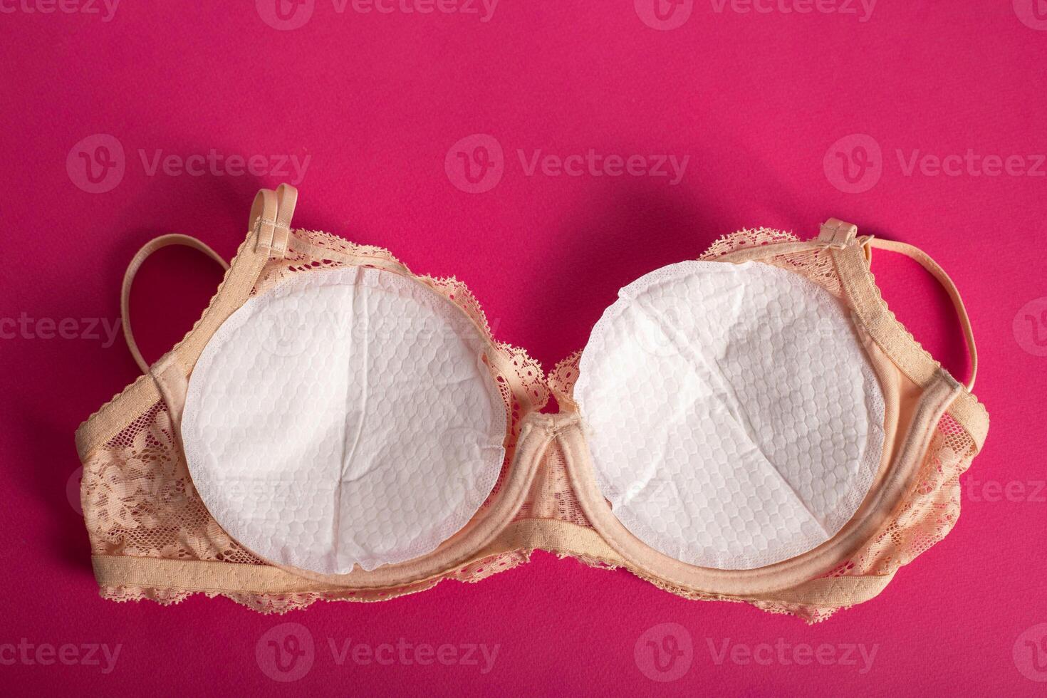 Women's bra with liners against the flow of milk from the breast of a nursing woman on a pink background. photo