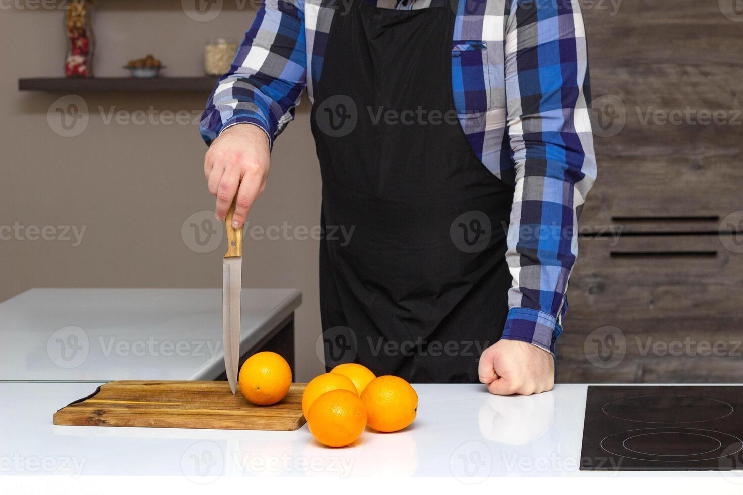 A man in an apron chef stands with a knife in the kitchen, oranges fruits are on the table, copy space, lifestyle photo
