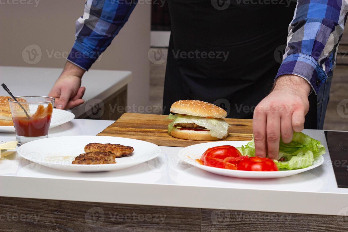 Male cook preparing cheeseburgers and hamburgers in the kitchen, on the table are the ingredients photo