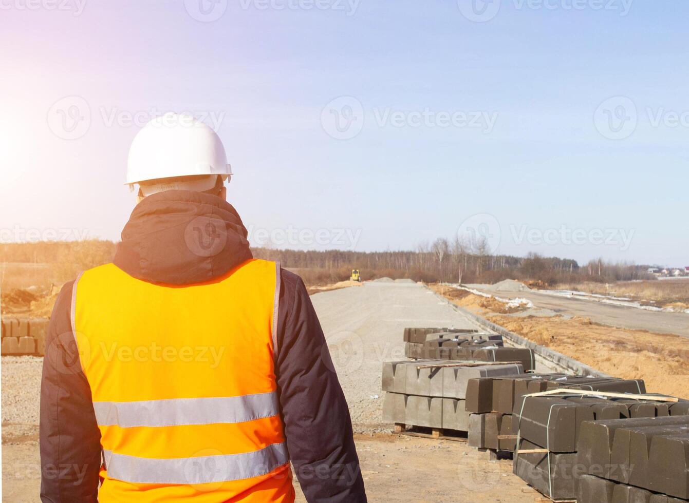 Chief engineer in a white helmet and signal vest against the background of the construction of a new road and curb, copy space, industry photo