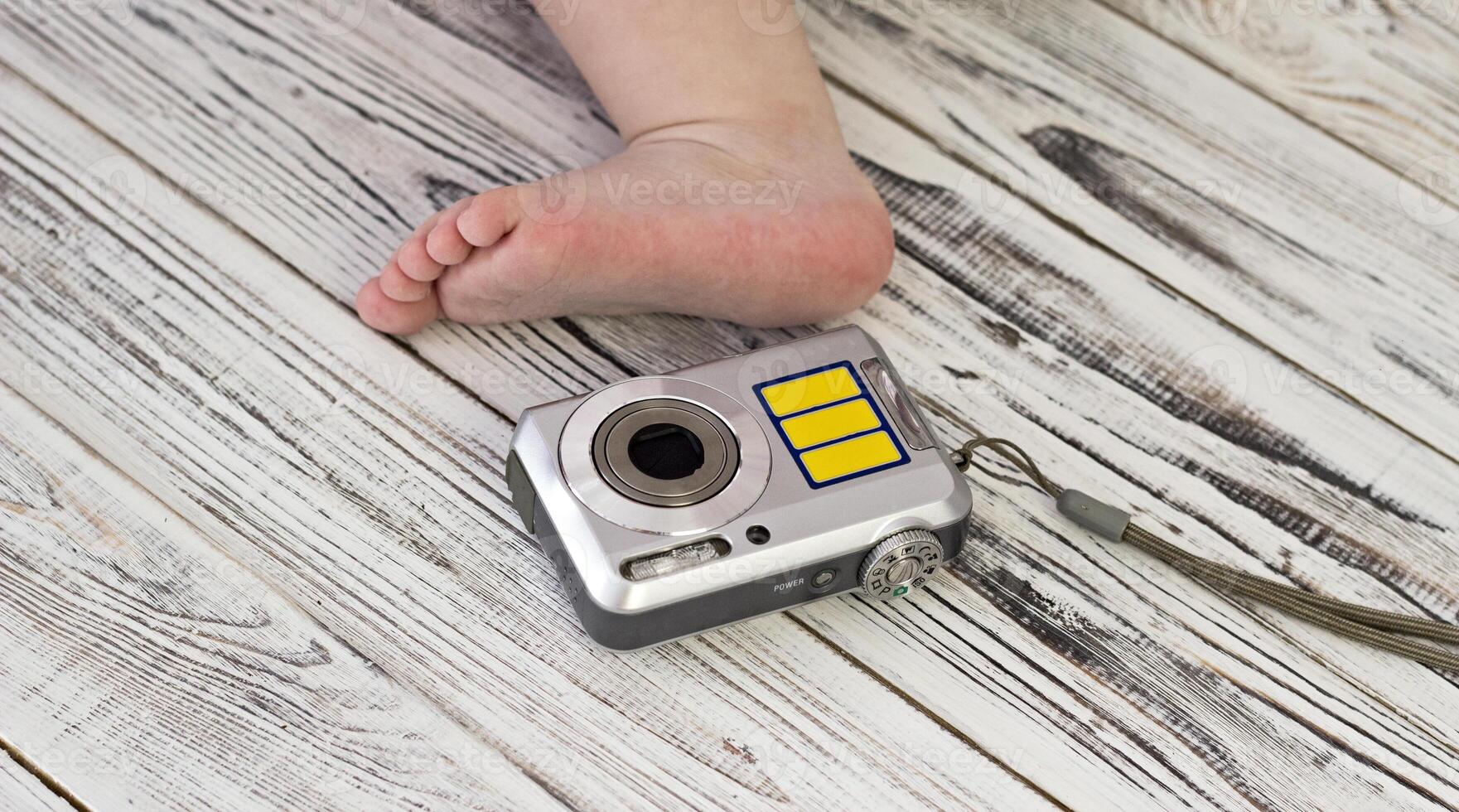 Baby foot and digital camera, white wooden background, close-up photo