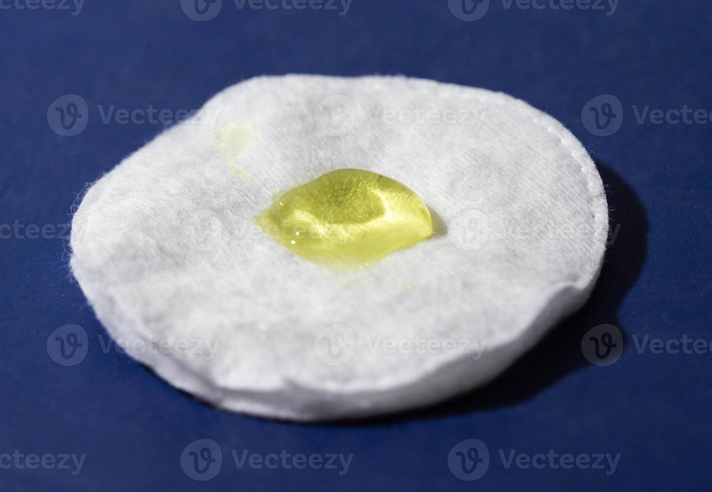 Medical healing ointment of yellow color on a white cotton pad and a blue background. Warming anesthetic ointment for the treatment of bruises, macro photo
