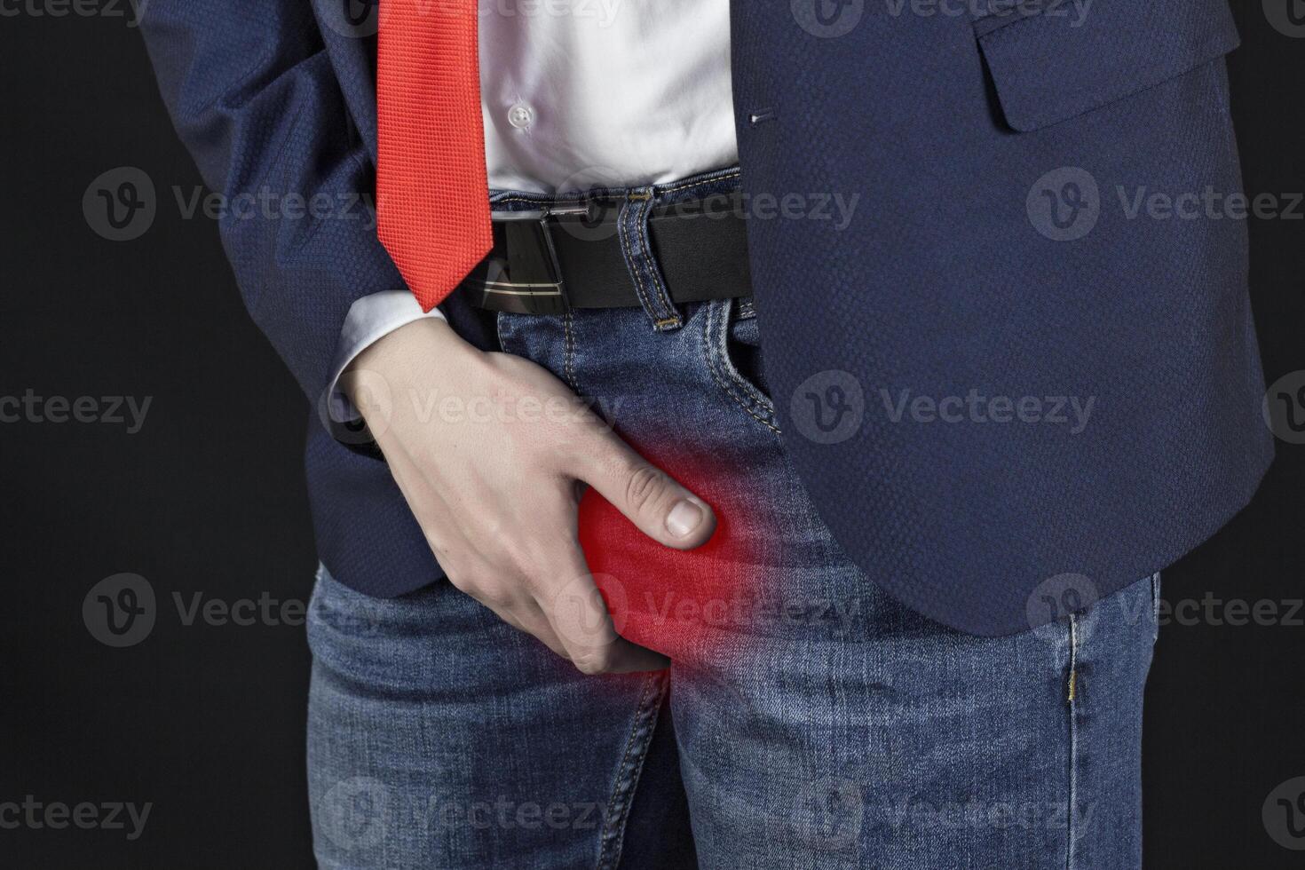 A man in a punch jacket and a necktie is a businessman holds on the groin, a black background photo