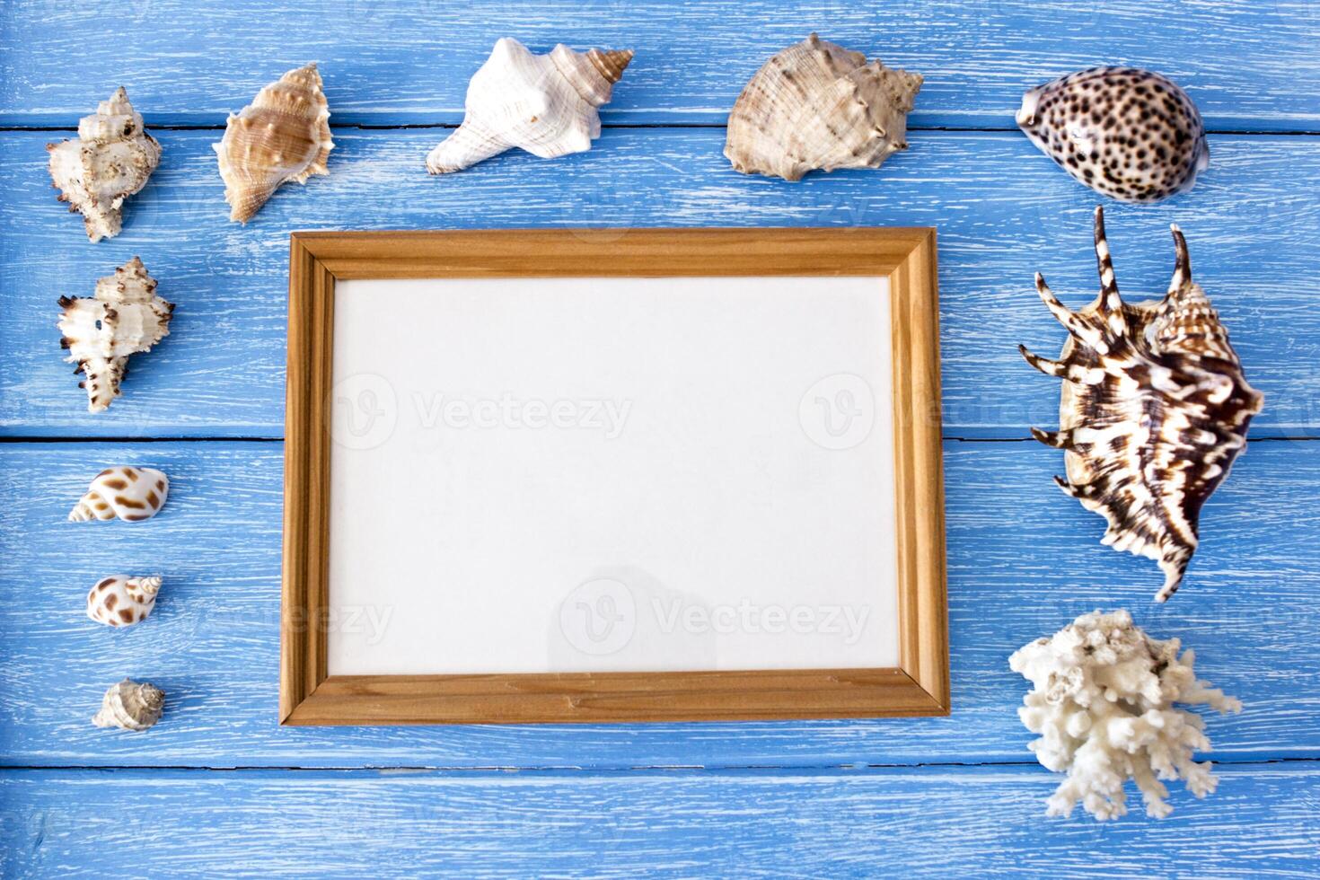 Sea shells and frame on a blue wooden background, blank frame for an inscription photo