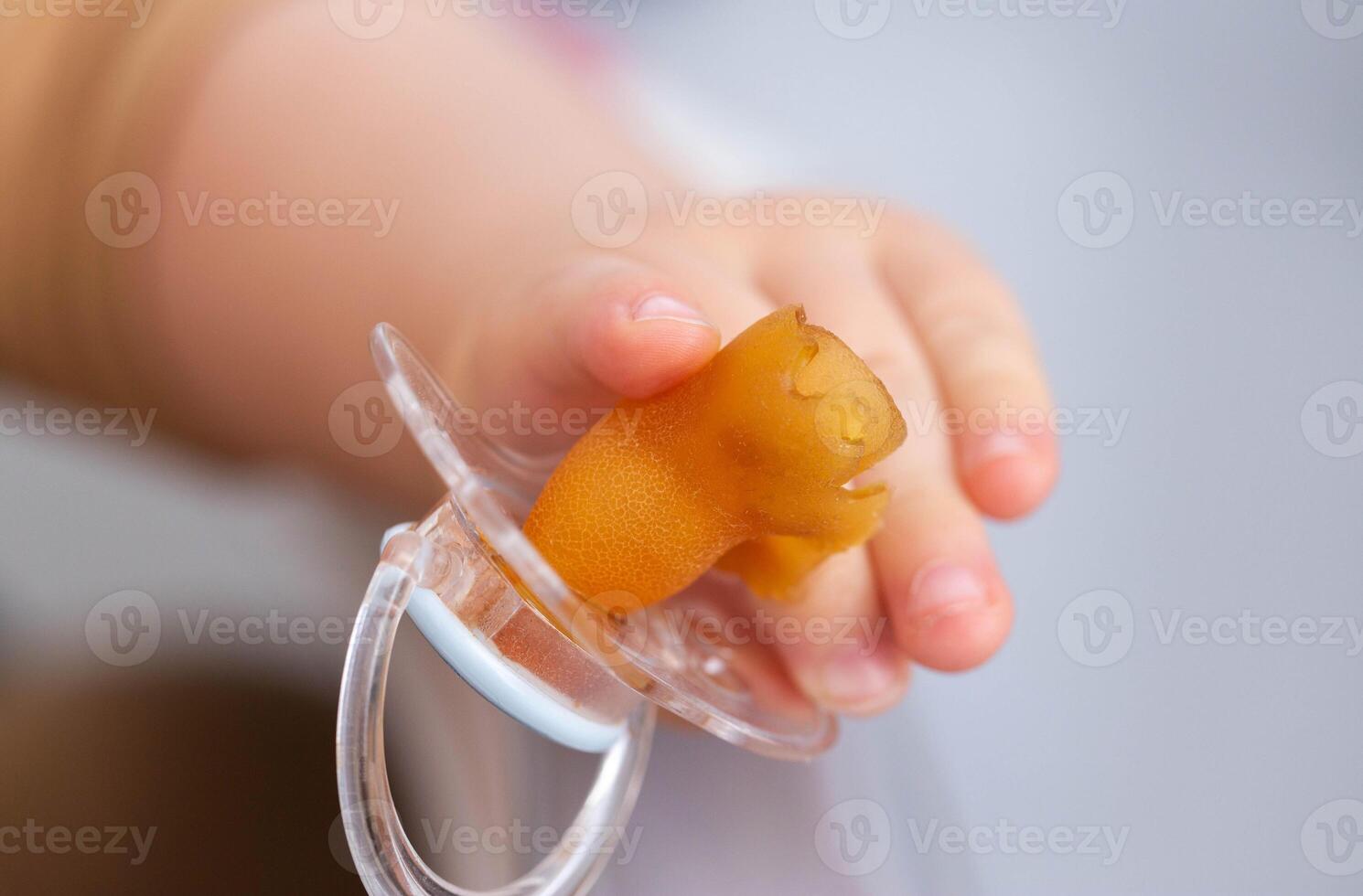 A baby's pacifier is chewed and torn in a baby's hand, close-up. Concept of teething in children, problems with bite. Copy space for text photo