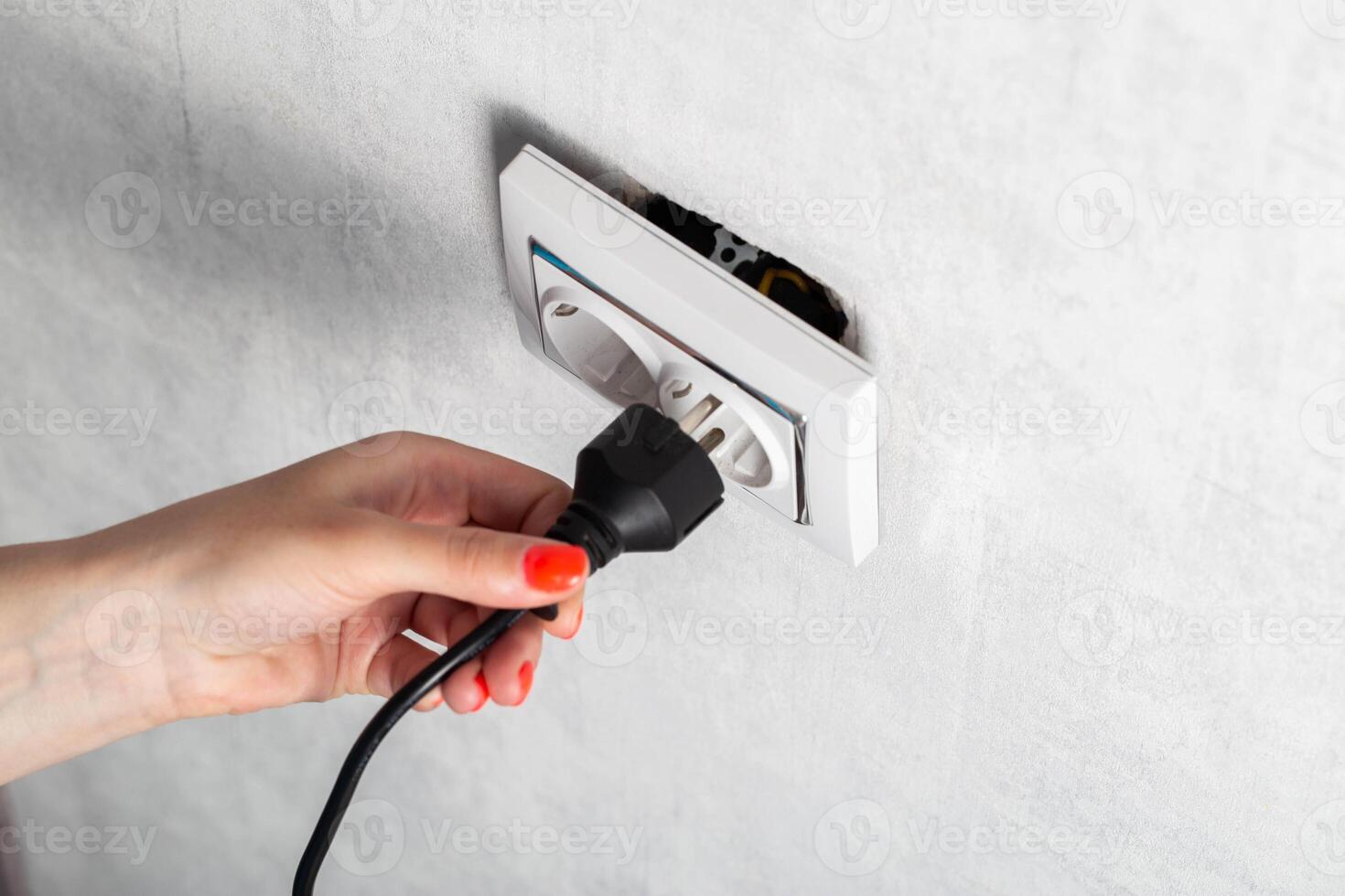 The girl puts the electric plug into a broken socket. Risk of electric shock, close-up photo
