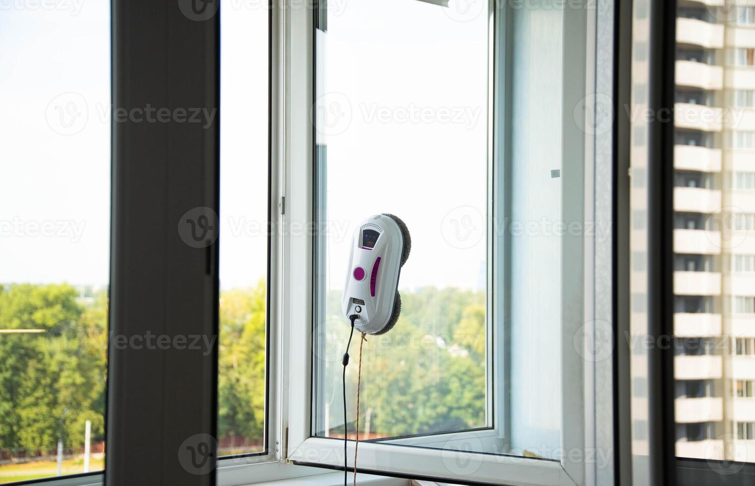 A modern vacuum robot window cleaner washes glass from dirt and stains on a pvc balcony frame. Fall safety. Copy space for text photo