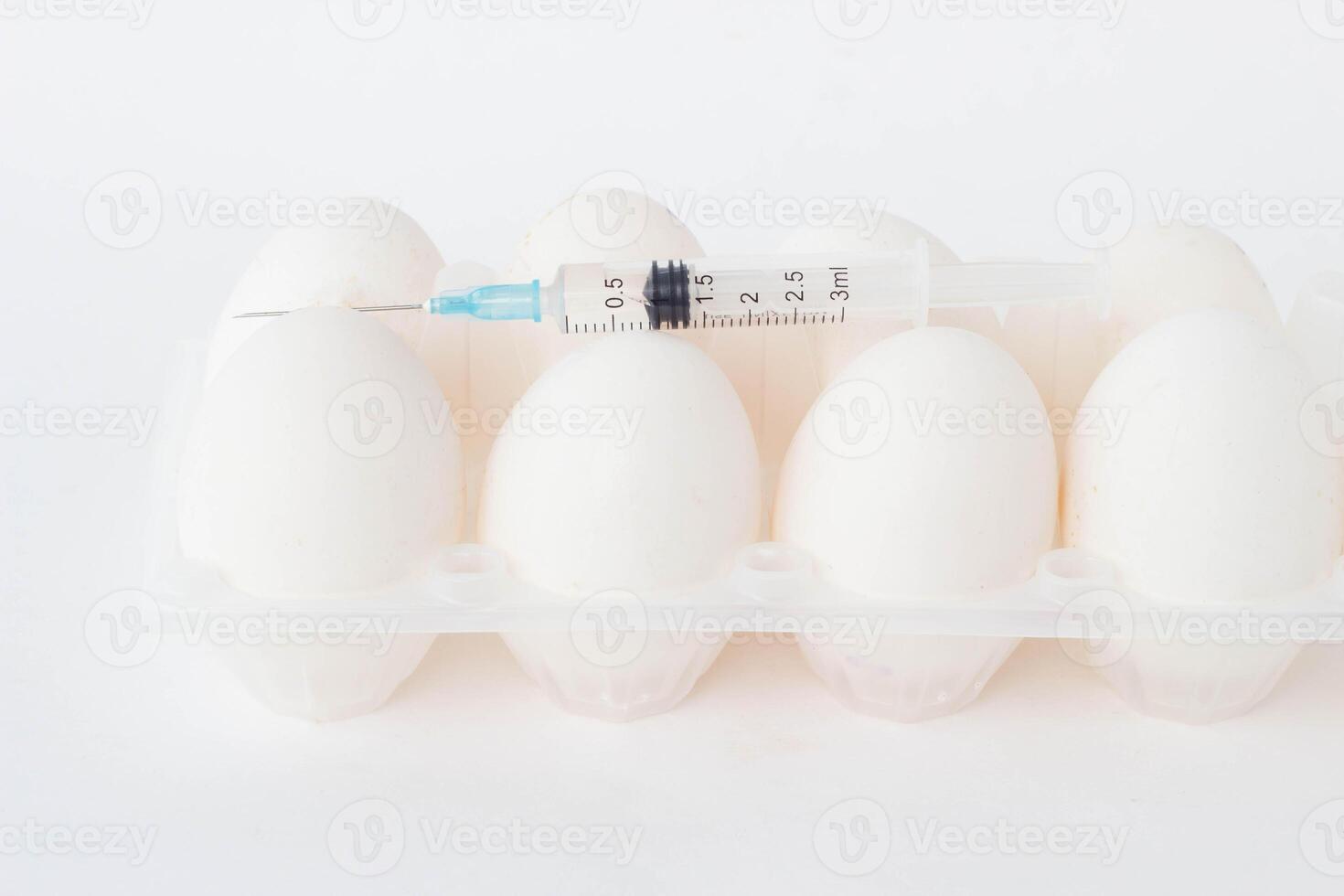 Chicken eggs on a white background on which lies a syringe in which there is a chemical substance, hormones, close-up photo
