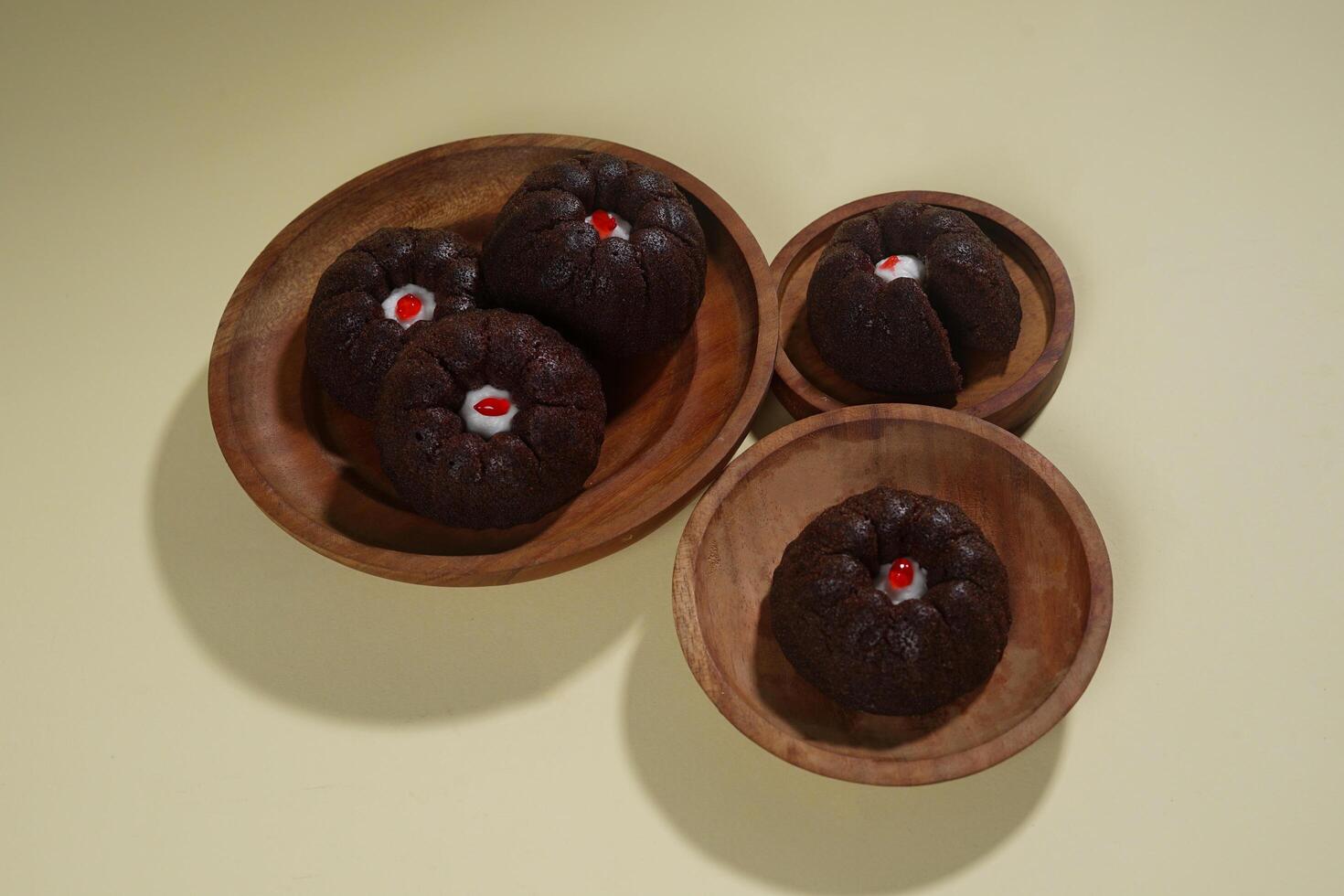 steamed brownie cake with a layer of red and white cream in the middle, served on a wooden plate isolated on yellow background photo