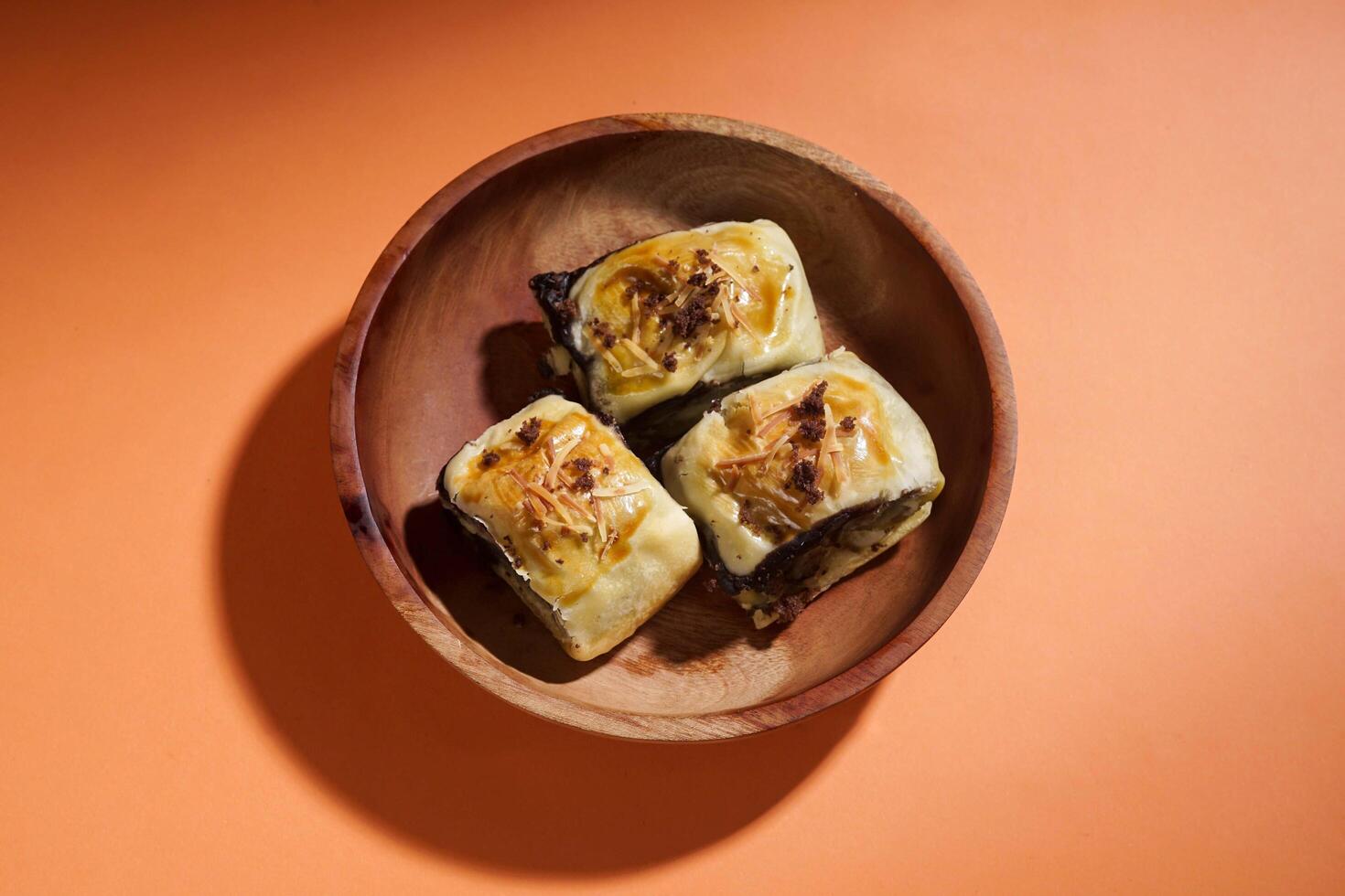 Banana Bolen is made from bananas and pastry dough, filled with chocolate and cheese. It is served on a wooden plate in a selective focus style image. photo