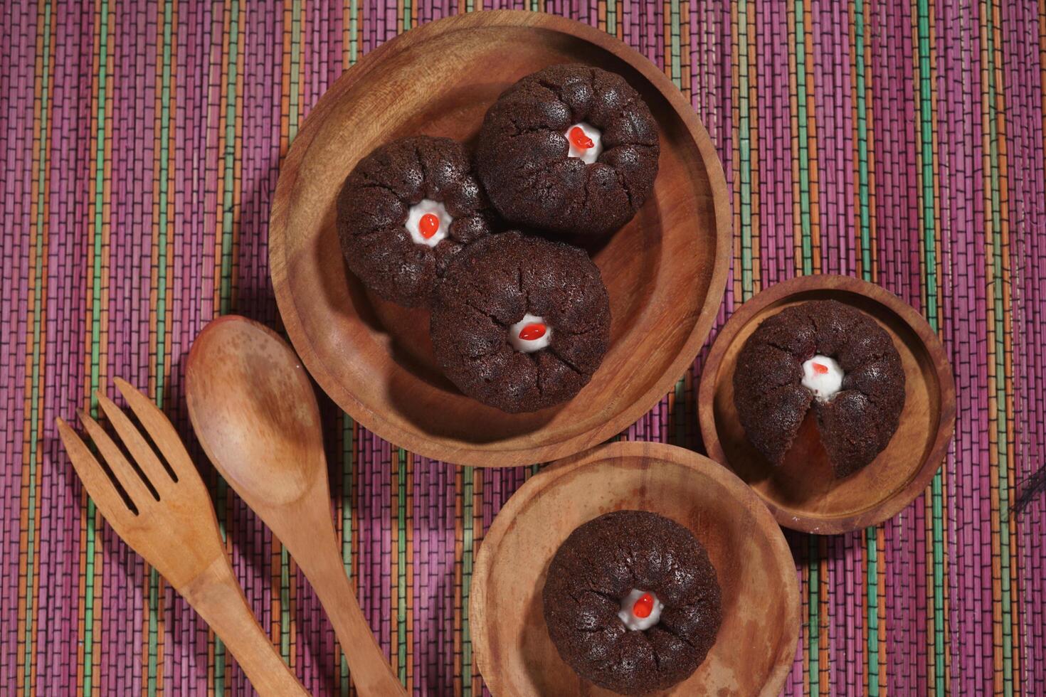 steamed brownie cake with a layer of red and white cream in the middle, served on a wooden plate placed on a rainbow-colored mat photo