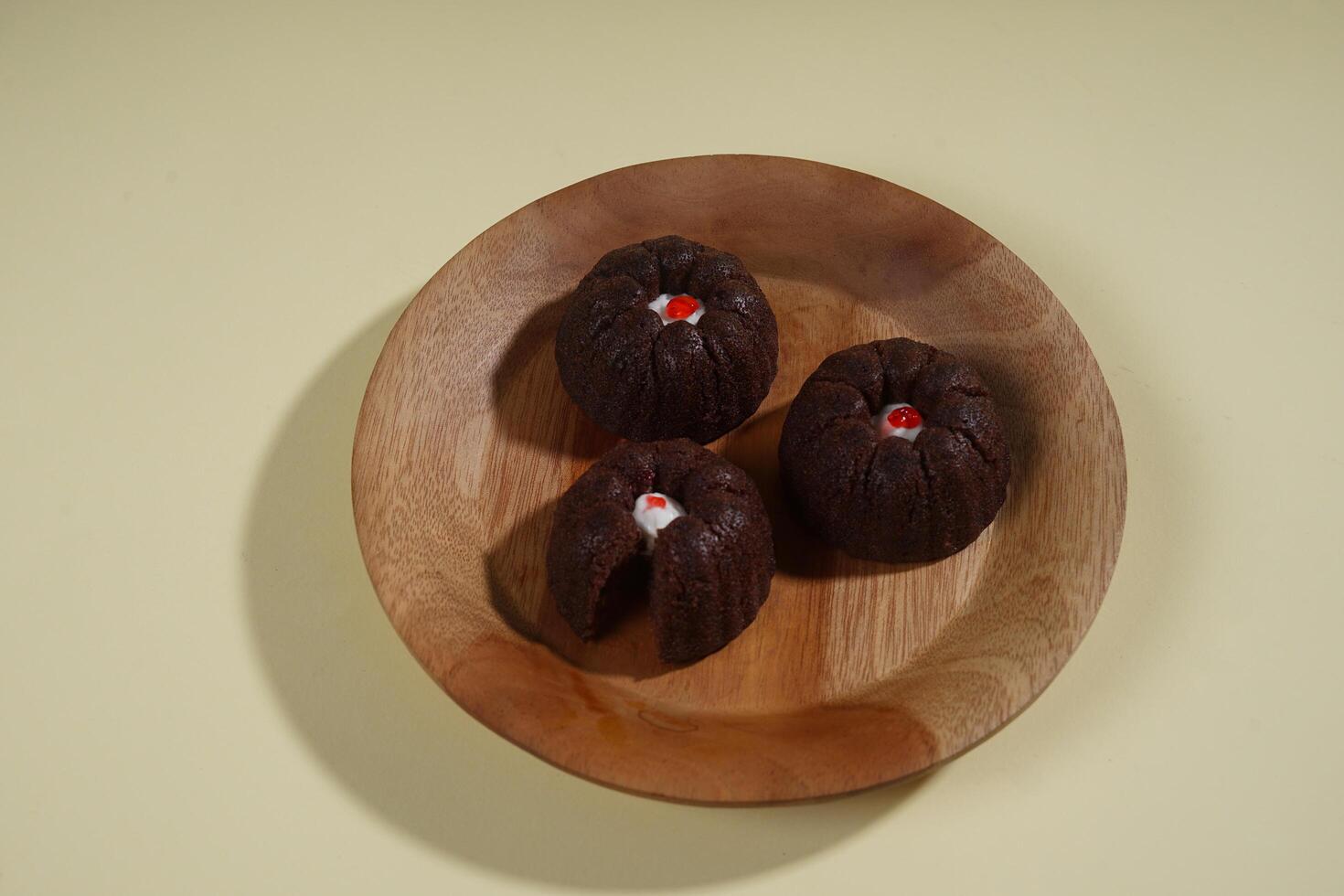 steamed brownie cake with a layer of red and white cream in the middle, served on a wooden plate isolated on yellow background photo