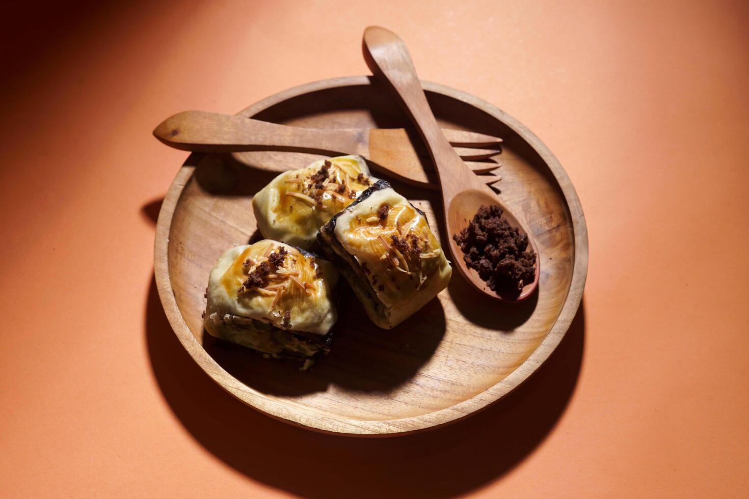 Banana Bolen is made from bananas and pastry dough, filled with chocolate and cheese. It is served on a wooden plate in a selective focus style image. photo