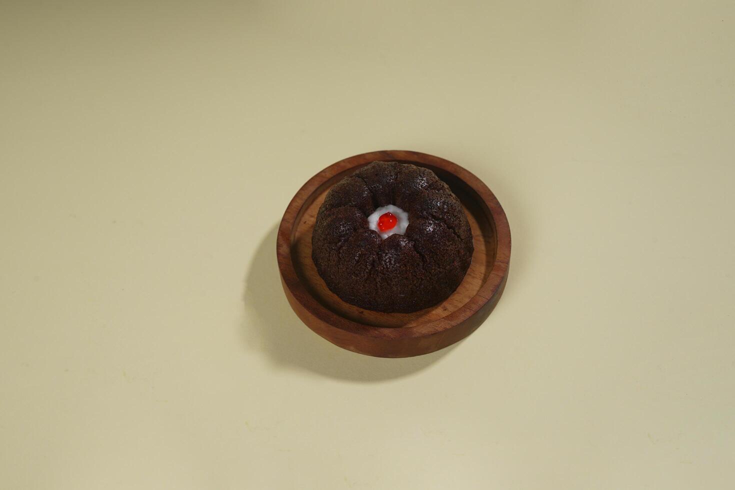 steamed brownie cake with a layer of red and white cream in the middle, served on a wooden plate isolated on yellow background photo