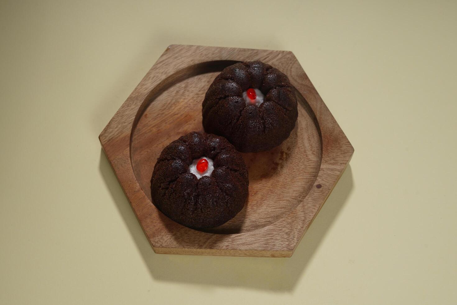 steamed brownie cake with a layer of red and white cream in the middle, served on a wooden plate isolated on yellow background photo