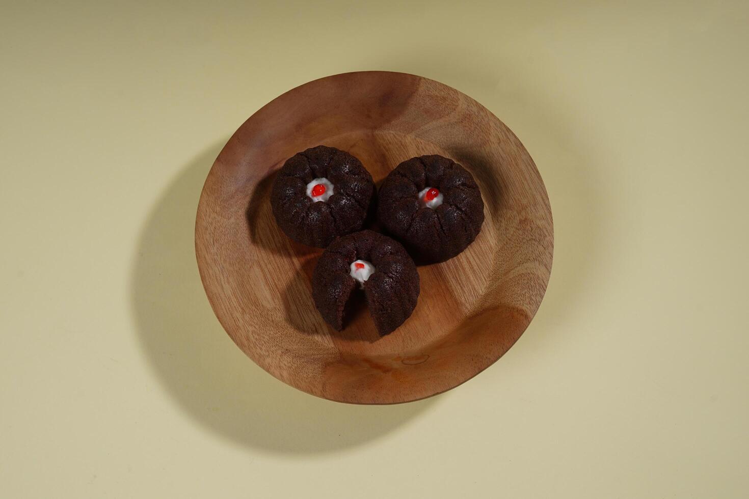 steamed brownie cake with a layer of red and white cream in the middle, served on a wooden plate isolated on yellow background photo