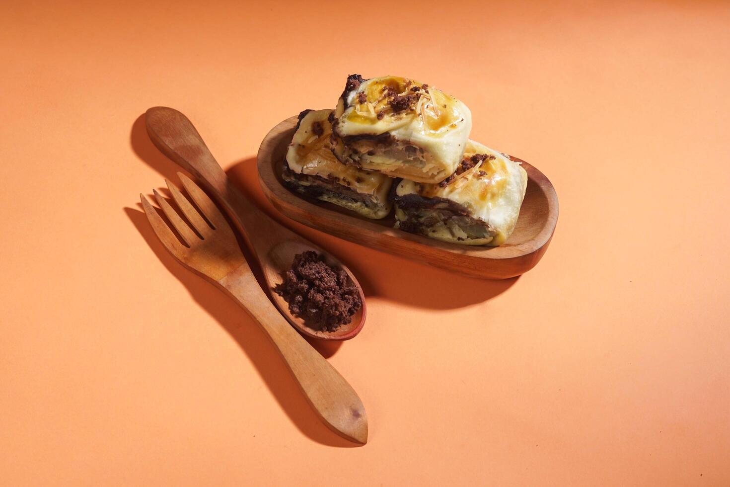 Banana Bolen is made from bananas and pastry dough, filled with chocolate and cheese. It is served on a wooden plate in a selective focus style image. photo