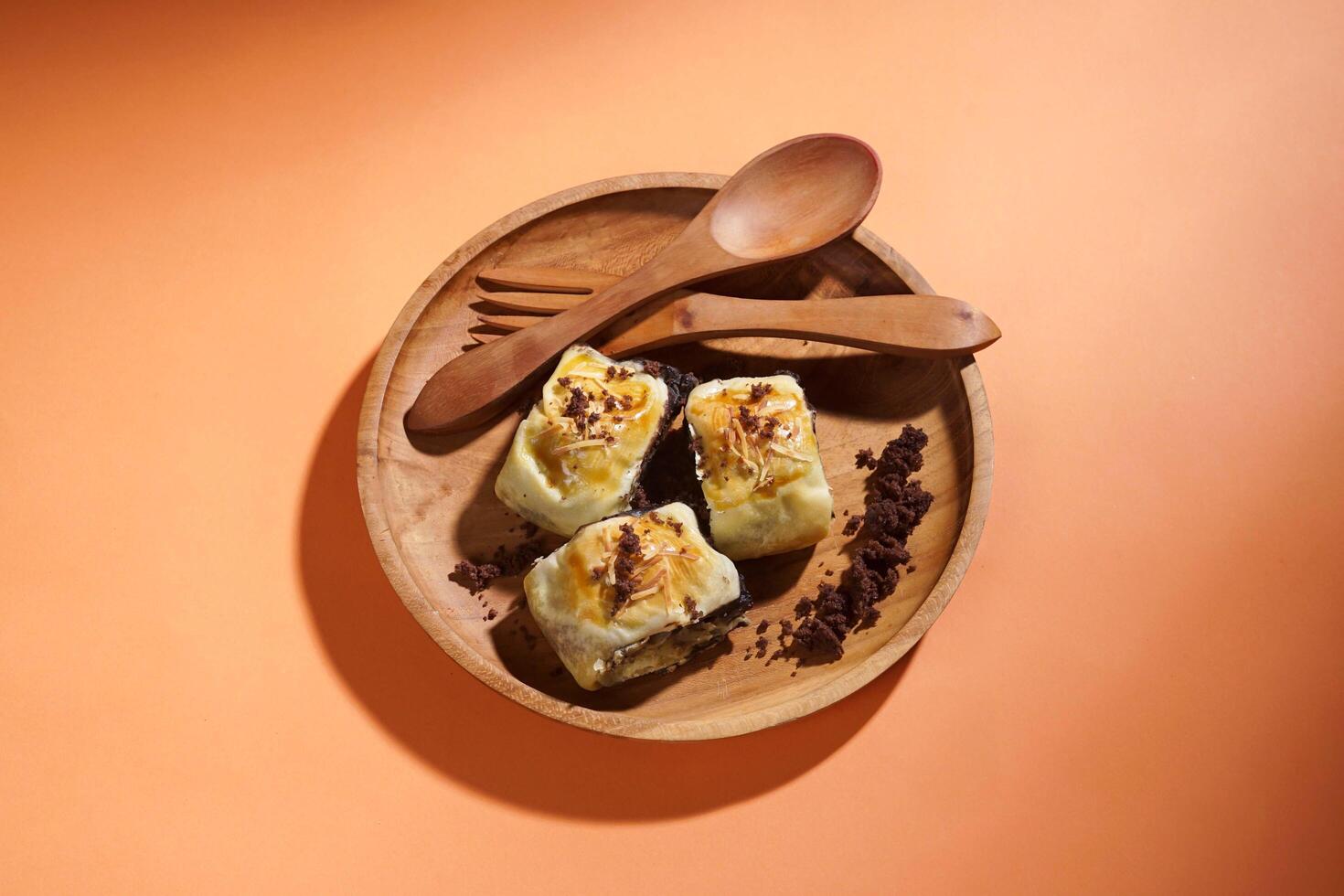Banana Bolen is made from bananas and pastry dough, filled with chocolate and cheese. It is served on a wooden plate in a selective focus style image. photo
