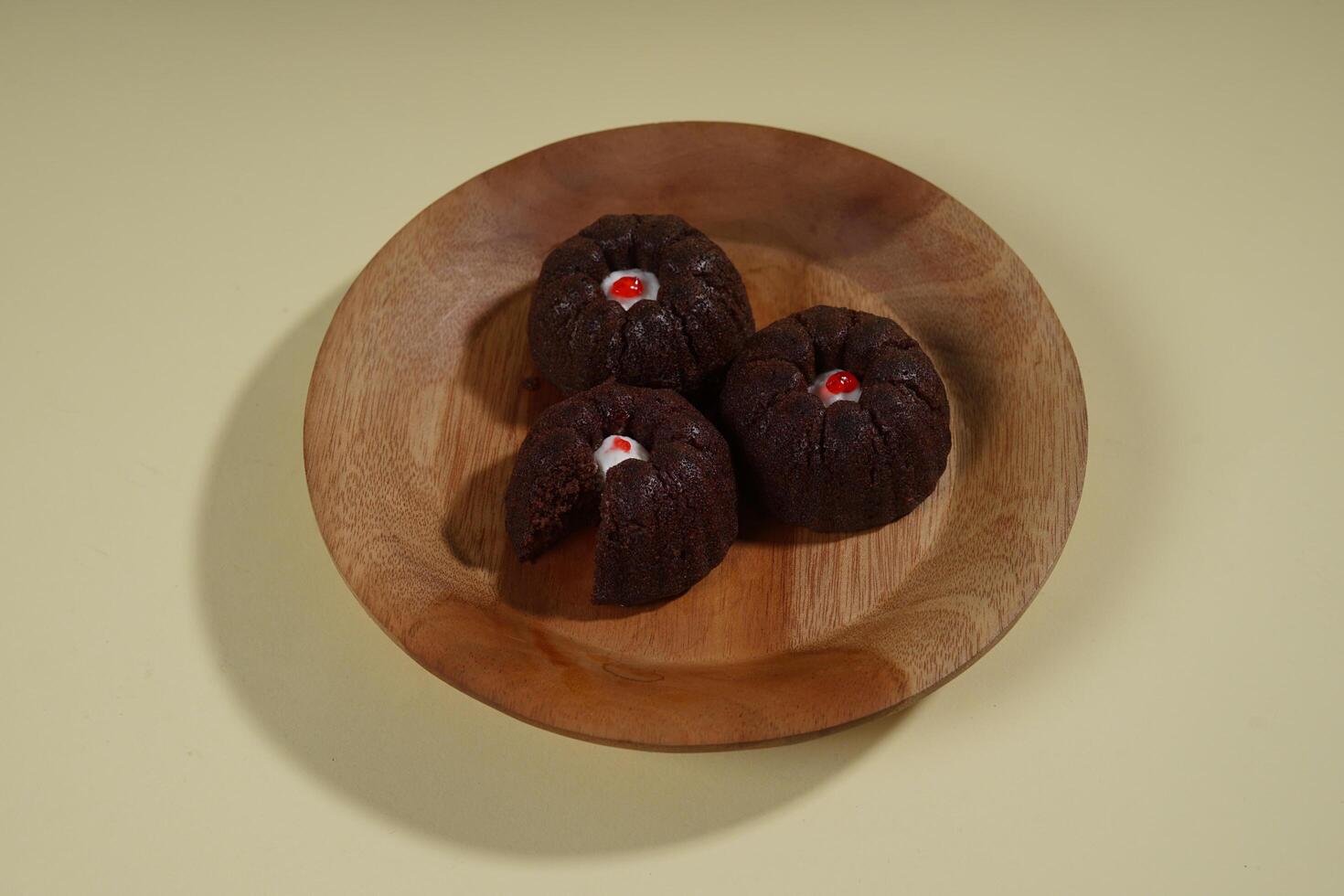 steamed brownie cake with a layer of red and white cream in the middle, served on a wooden plate isolated on yellow background photo