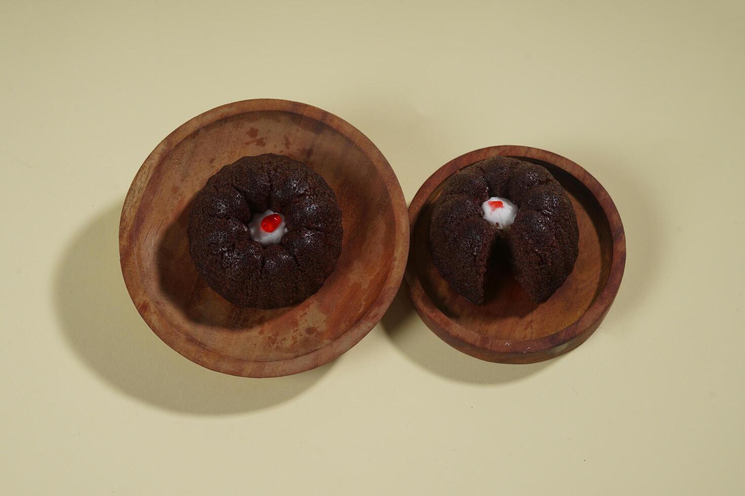 steamed brownie cake with a layer of red and white cream in the middle, served on a wooden plate isolated on yellow background photo