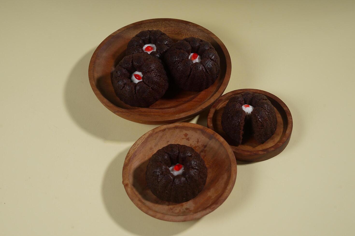 steamed brownie cake with a layer of red and white cream in the middle, served on a wooden plate isolated on yellow background photo