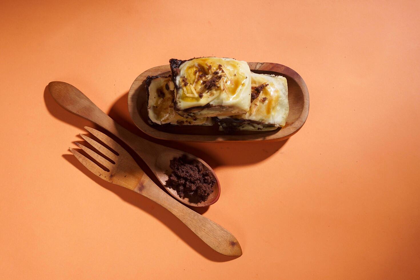 Banana Bolen is made from bananas and pastry dough, filled with chocolate and cheese. It is served on a wooden plate in a selective focus style image. photo