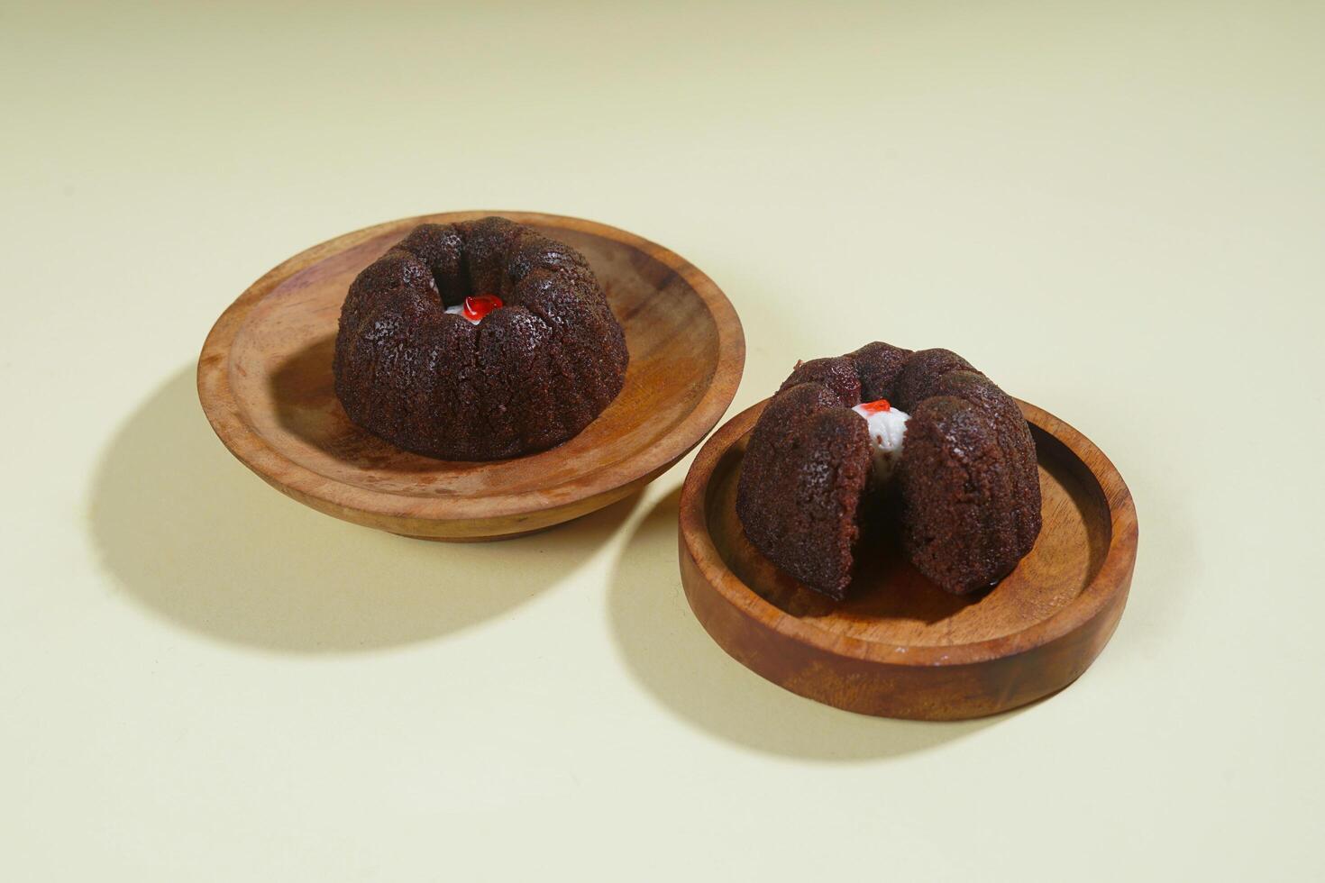 steamed brownie cake with a layer of red and white cream in the middle, served on a wooden plate isolated on yellow background photo