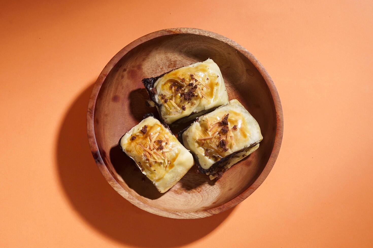 Banana Bolen is made from bananas and pastry dough, filled with chocolate and cheese. It is served on a wooden plate in a selective focus style image. photo