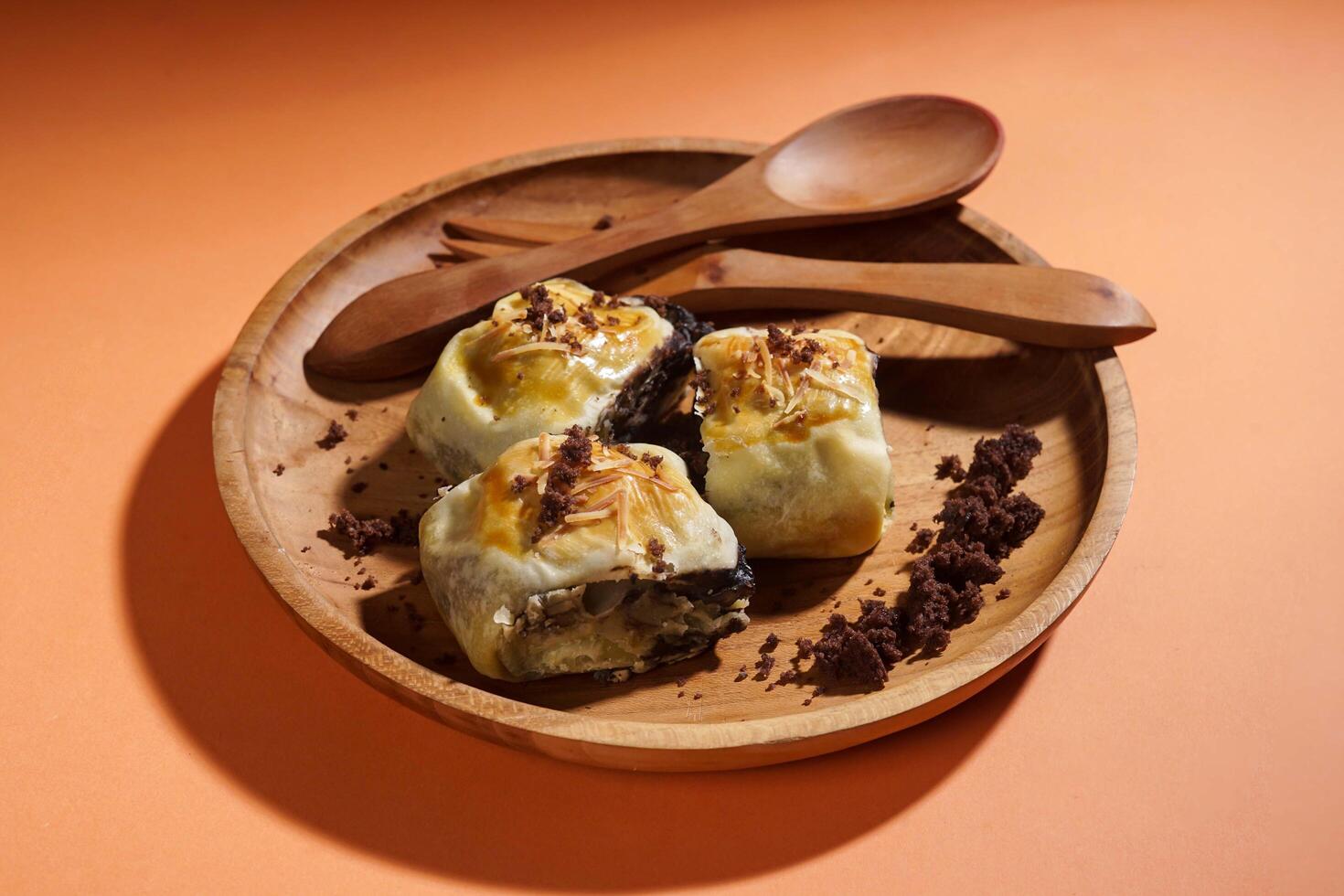 Banana Bolen is made from bananas and pastry dough, filled with chocolate and cheese. It is served on a wooden plate in a selective focus style image. photo