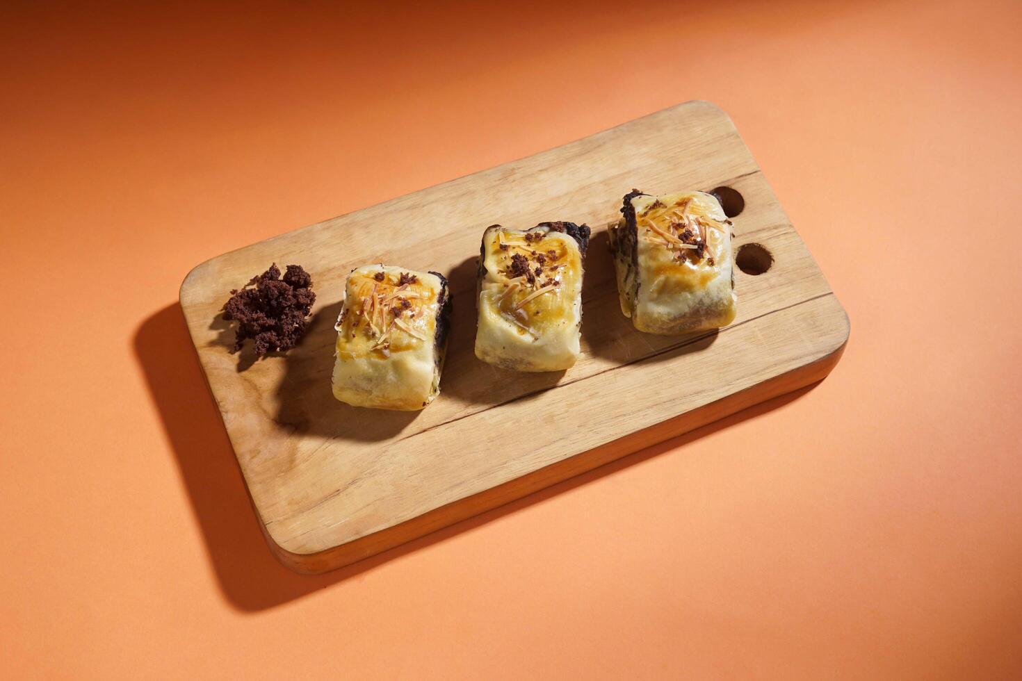 Banana Bolen is made from bananas and pastry dough, filled with chocolate and cheese. It is served on a wooden plate in a selective focus style image. photo