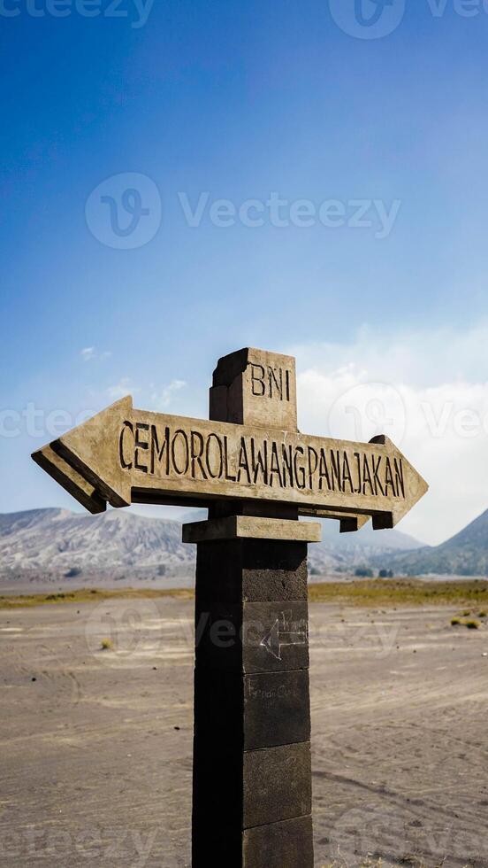 Stone sign post with opposite arrows and copy space, in Bromo volcano crater, dry landscape and dirt road in Java, Indonesia photo