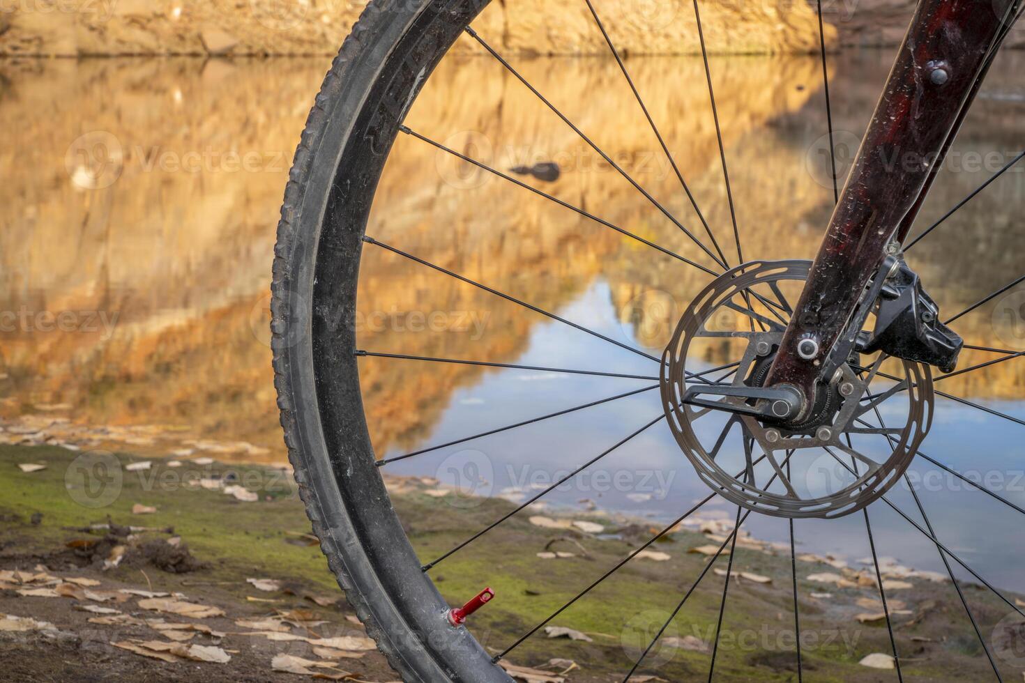 dirty front wheel of a gravel bike on a shore of lake with sandstone cliff reflection photo
