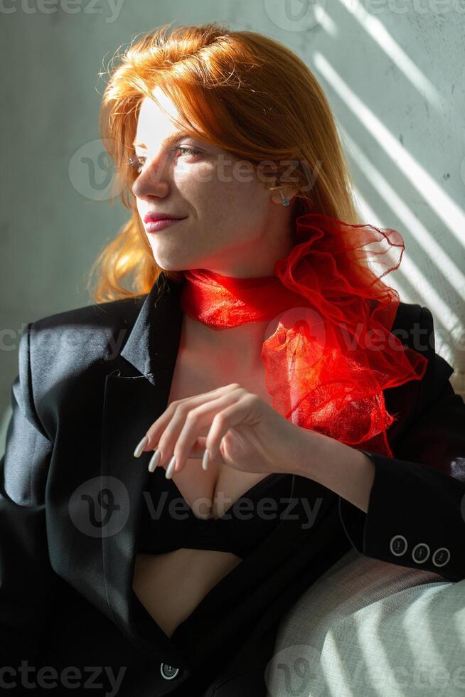 Portrait of a red-haired girl with a red scarf around her neck, in a suit and top, soft morning light. photo