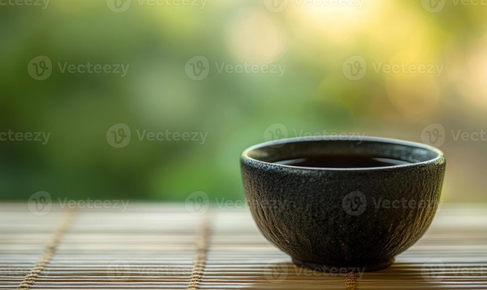 A black ceramic cup with a handle sits on a bamboo mat photo